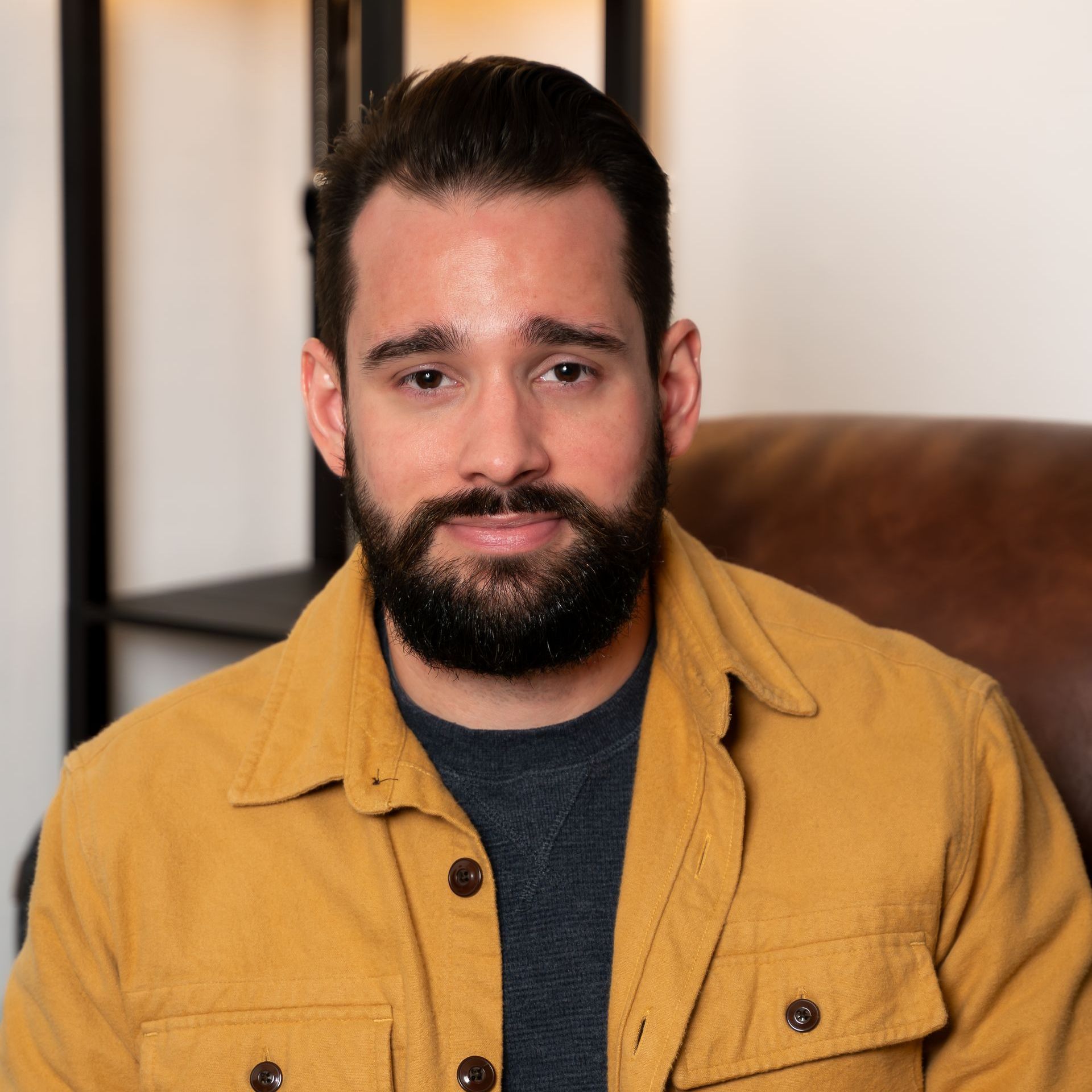 Headshot of a man in a blue suit and gray shirt is smiling for the camera .