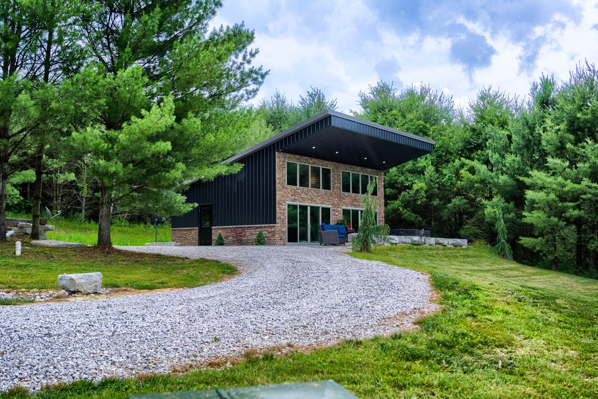 a small house in the middle of a forest with a gravel driveway leading to it .