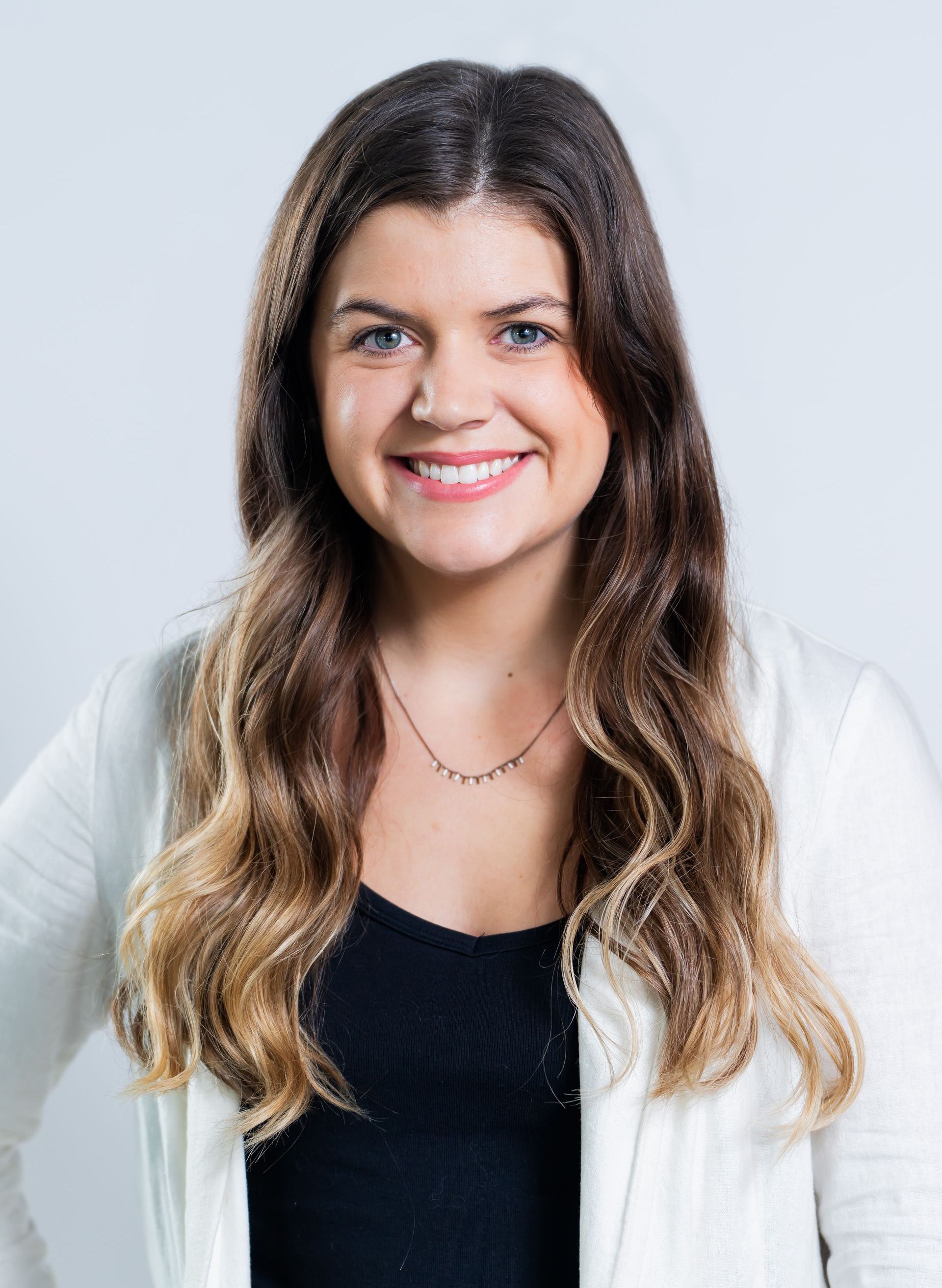 A woman wearing a white jacket and a black shirt is smiling for the camera.