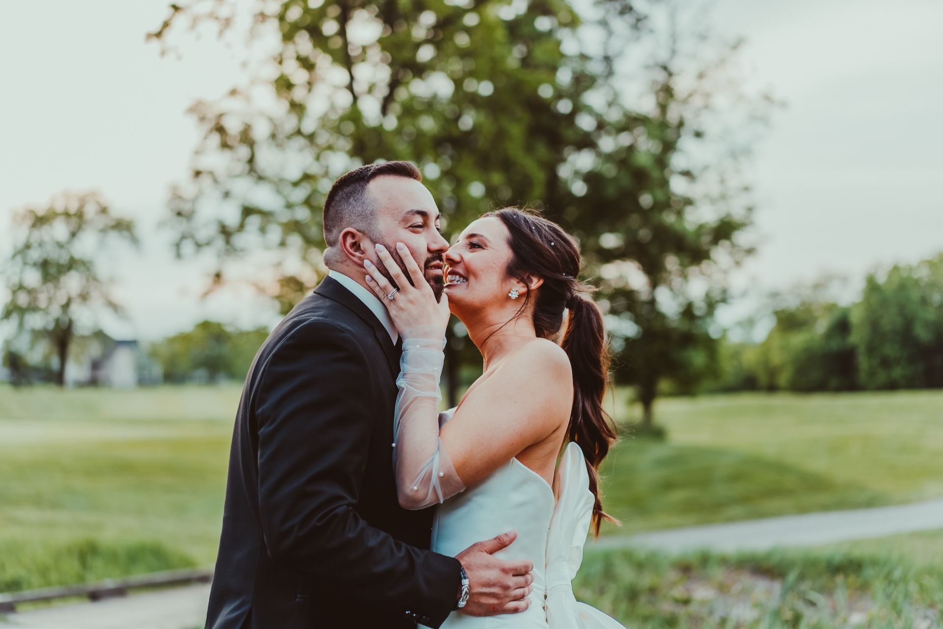 a bride and groom are kissing in a park .