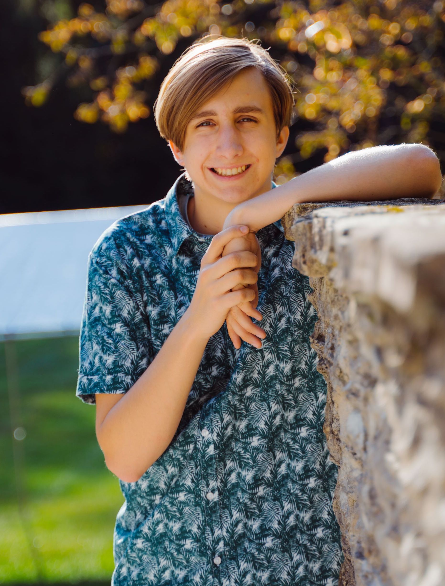 A high school senior is leaning against a stone wall and smiling .