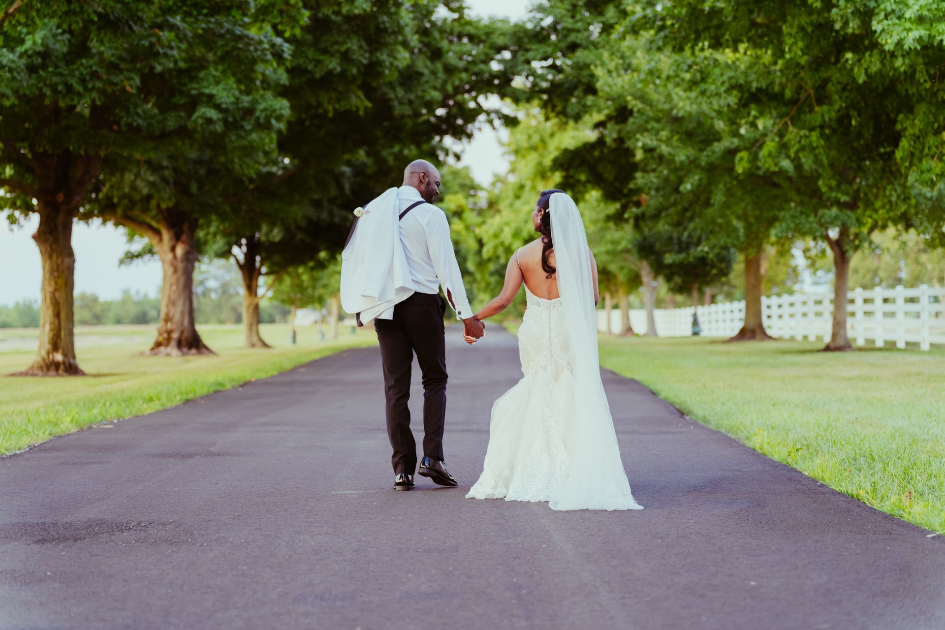 A bride and groom are walking down a path holding hands.