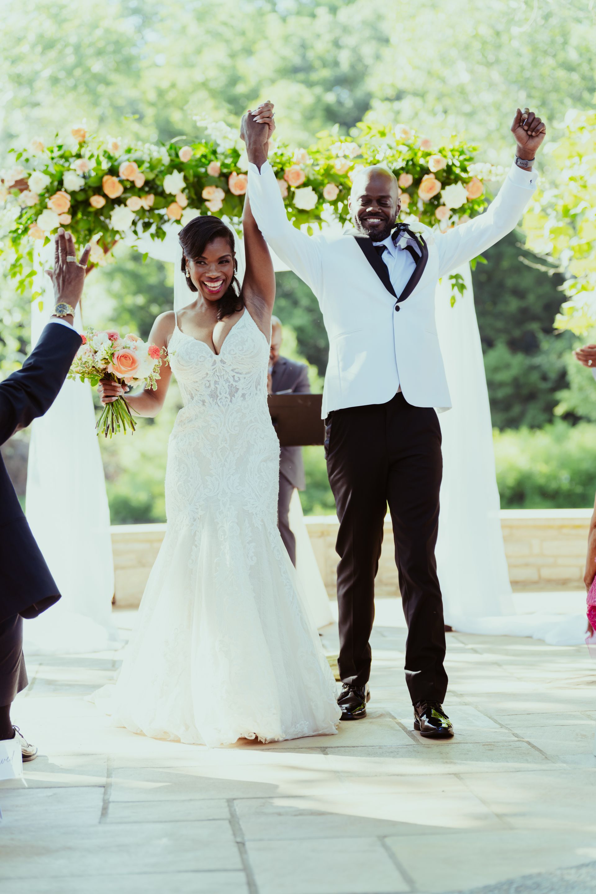 A bride and groom are celebrating their wedding with their hands in the air.