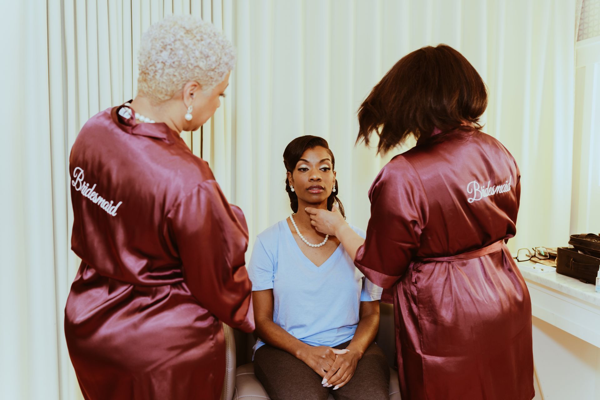 A woman is getting her hair done by two women in robes.