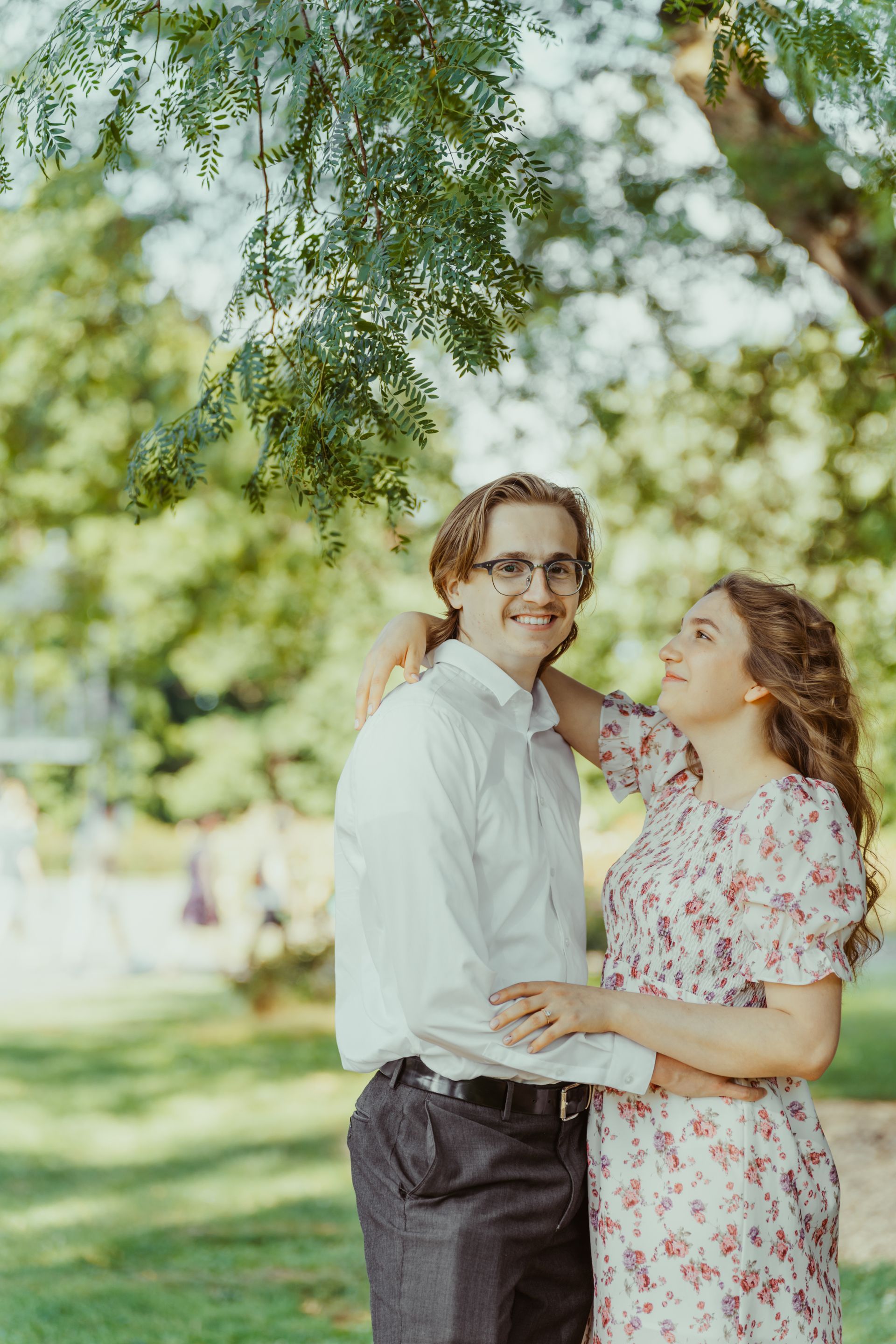 A man and a woman are standing under a tree in a park.