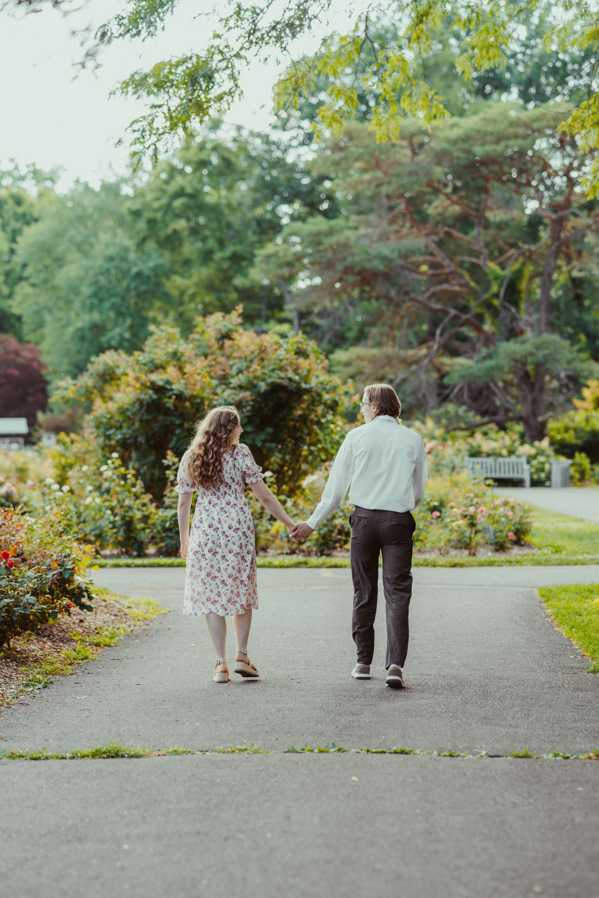 A man and a woman are walking down a path in a park holding hands.