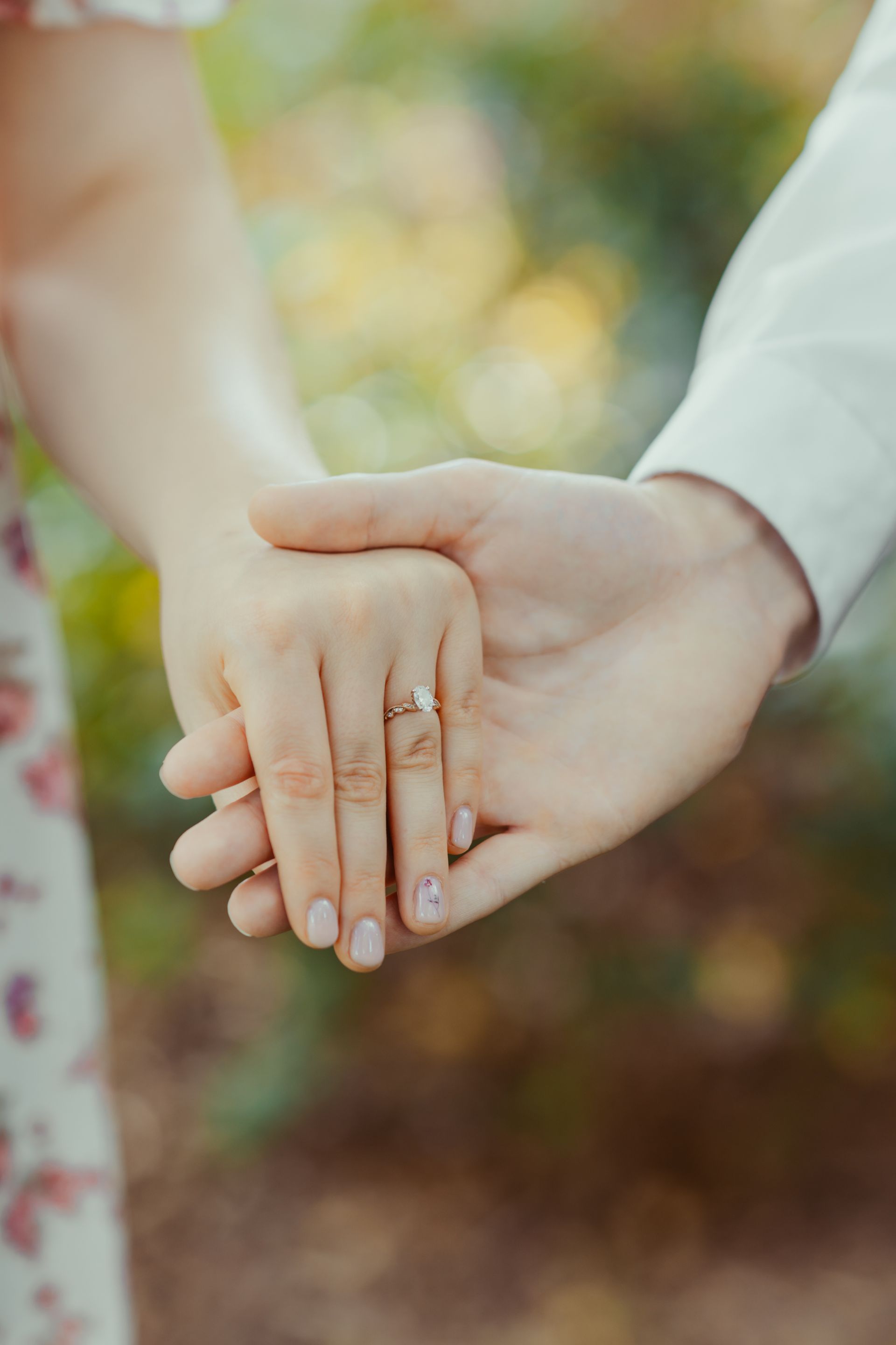 A man and a woman are holding hands and the woman is wearing an engagement ring.