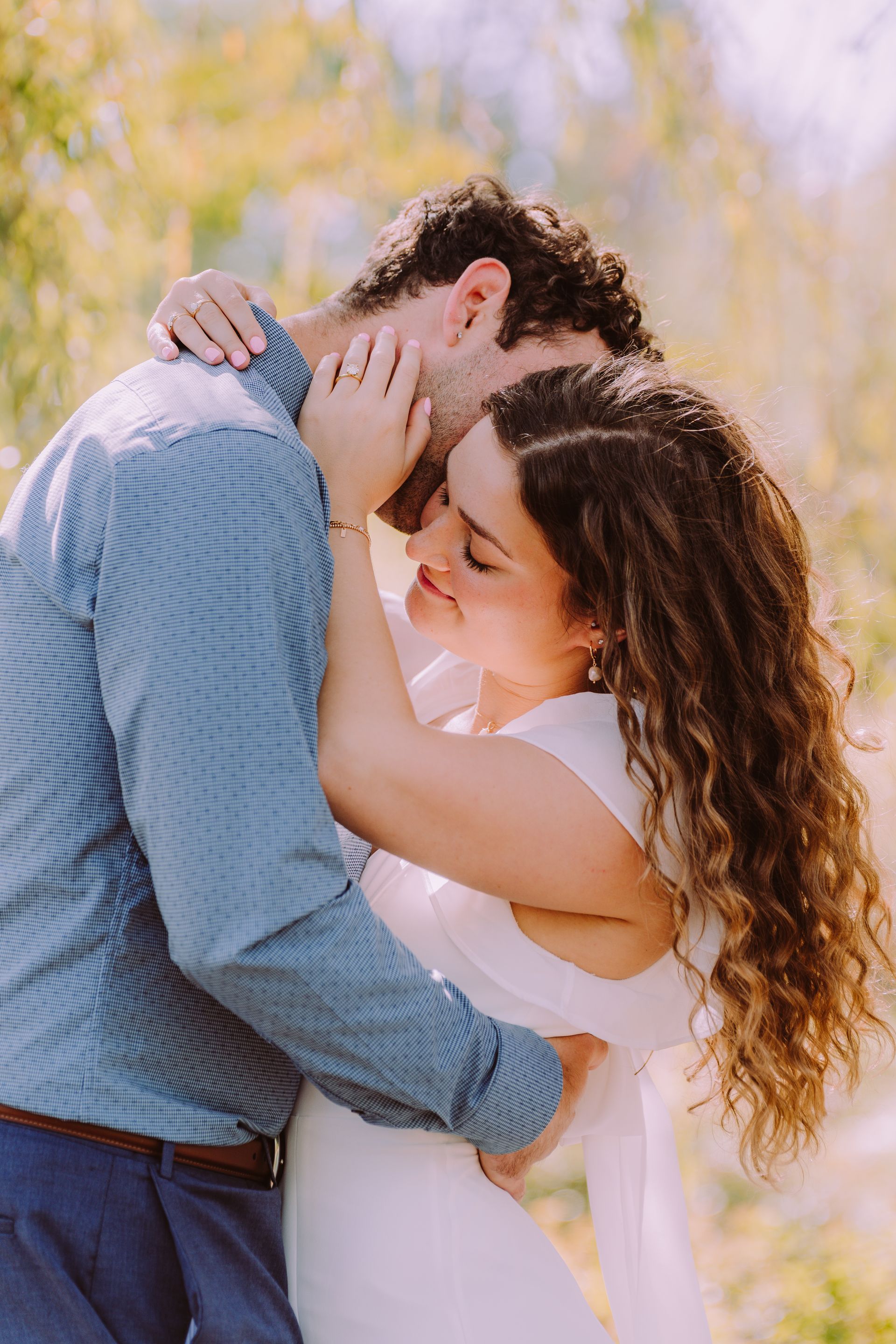 Couple embracing, man kissing woman's forehead, soft lighting, outdoor setting.