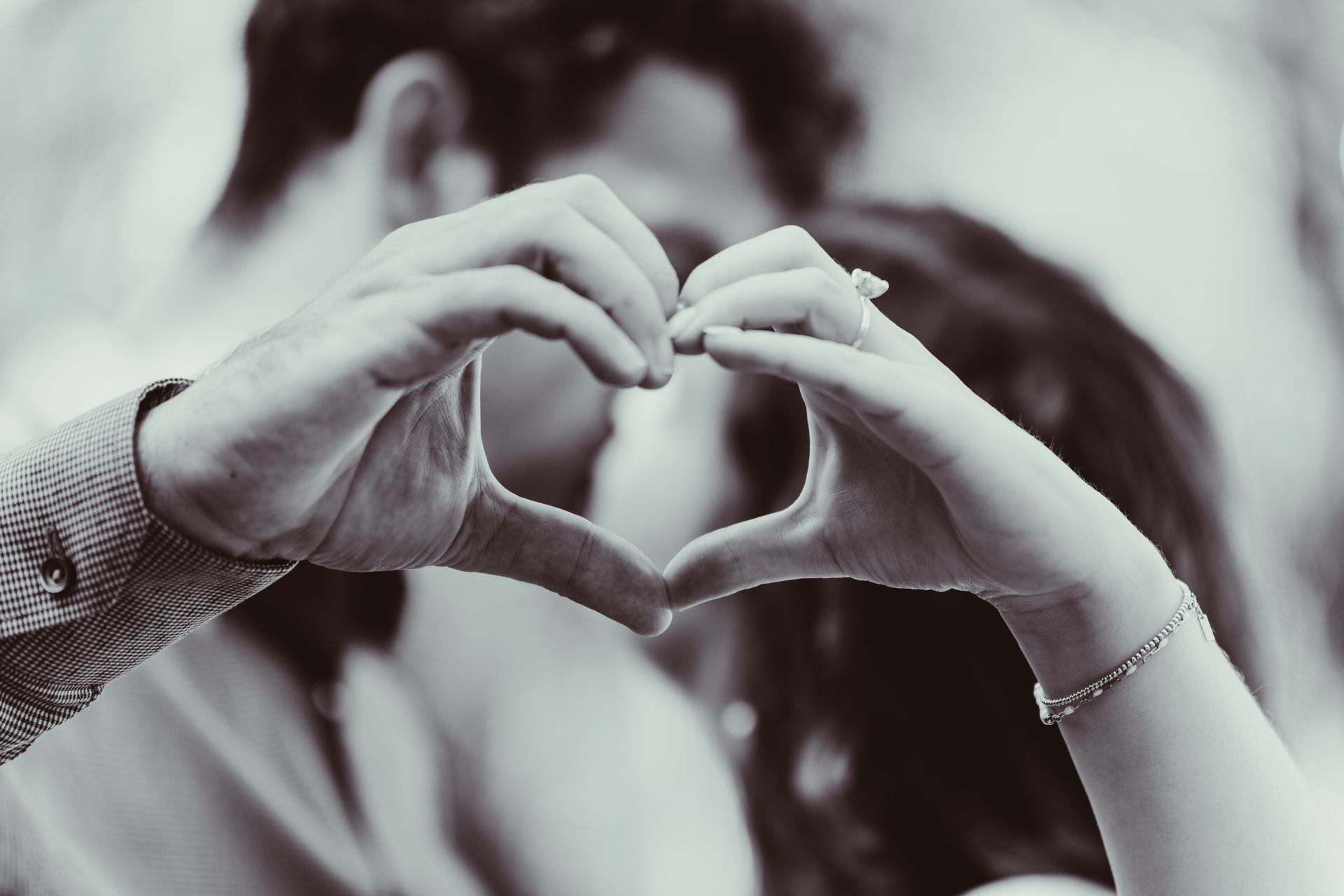 Couple forming a heart shape with their hands; one wears an engagement ring.