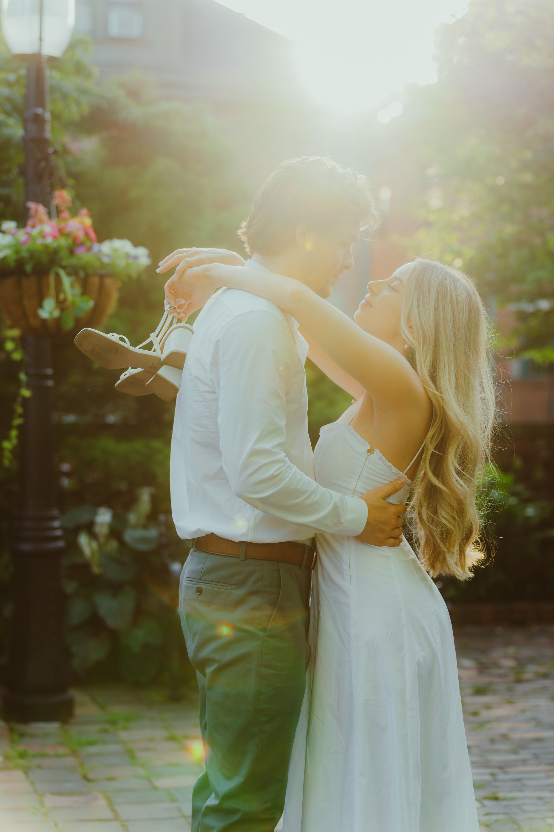 Couple embraces in sunlight, she in white dress, he in white shirt and green pants.