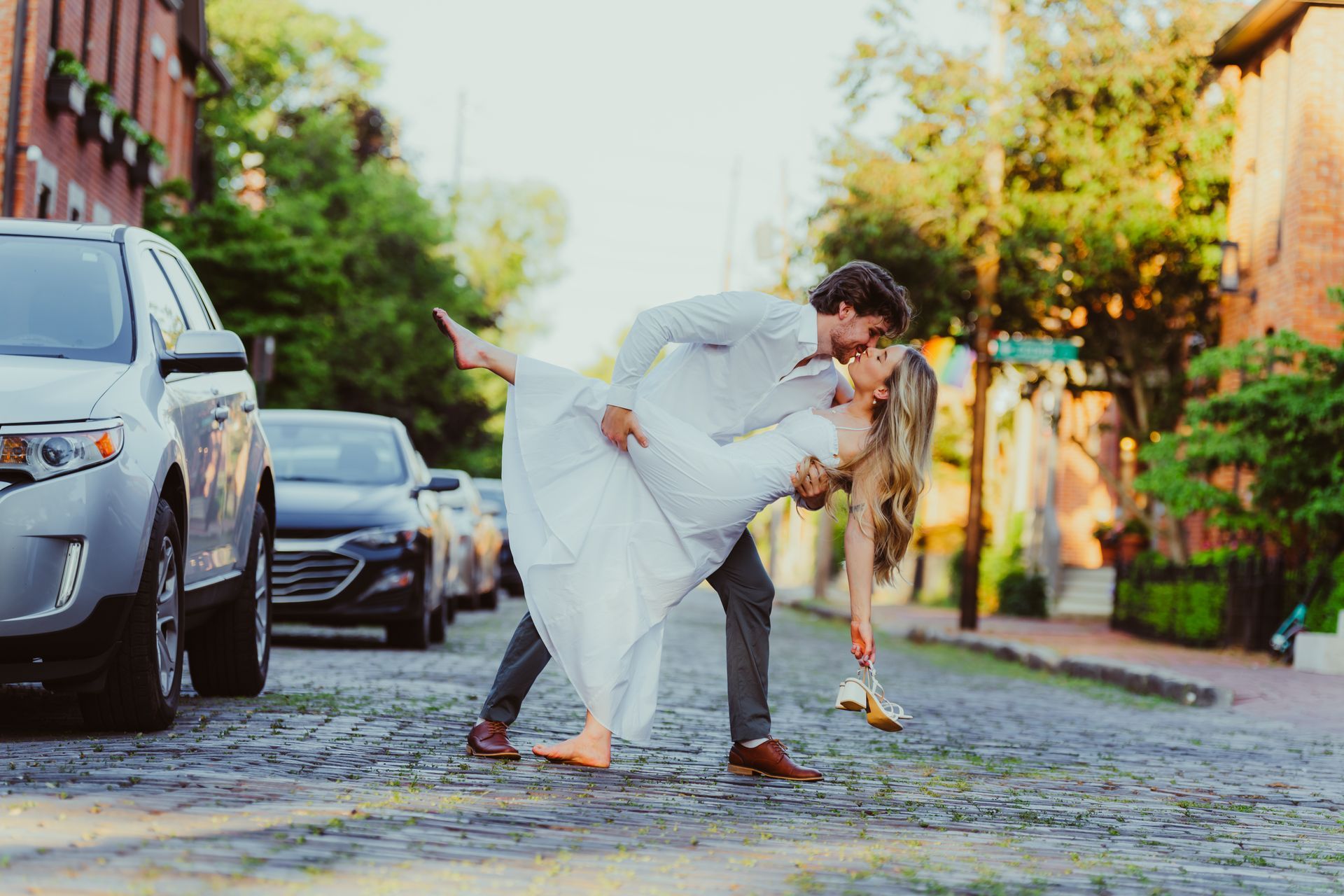 A bride and groom are kissing on a cobblestone street.