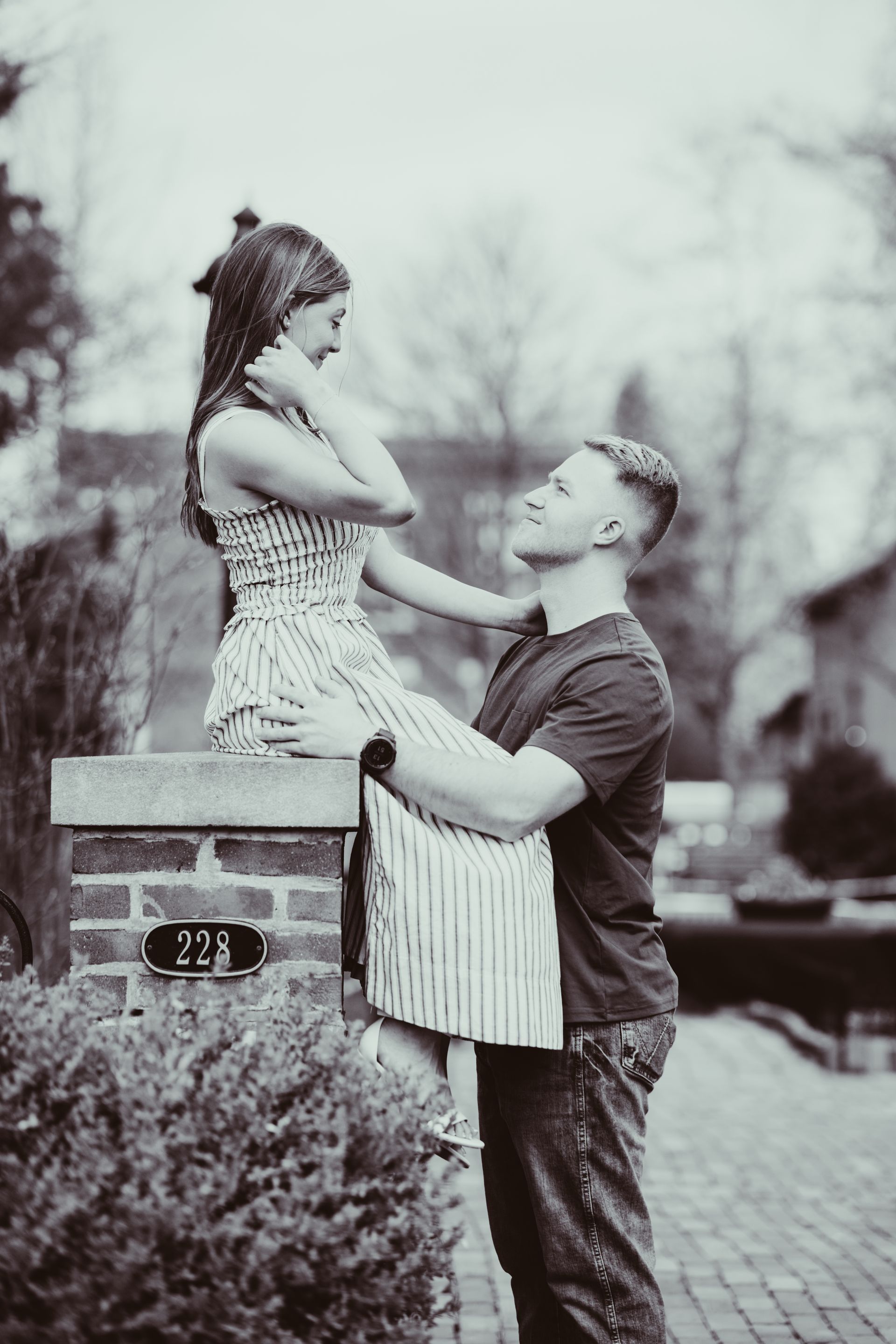 A person sits on a brick pillar while another stands facing them; they look at each other in an outdoor setting.