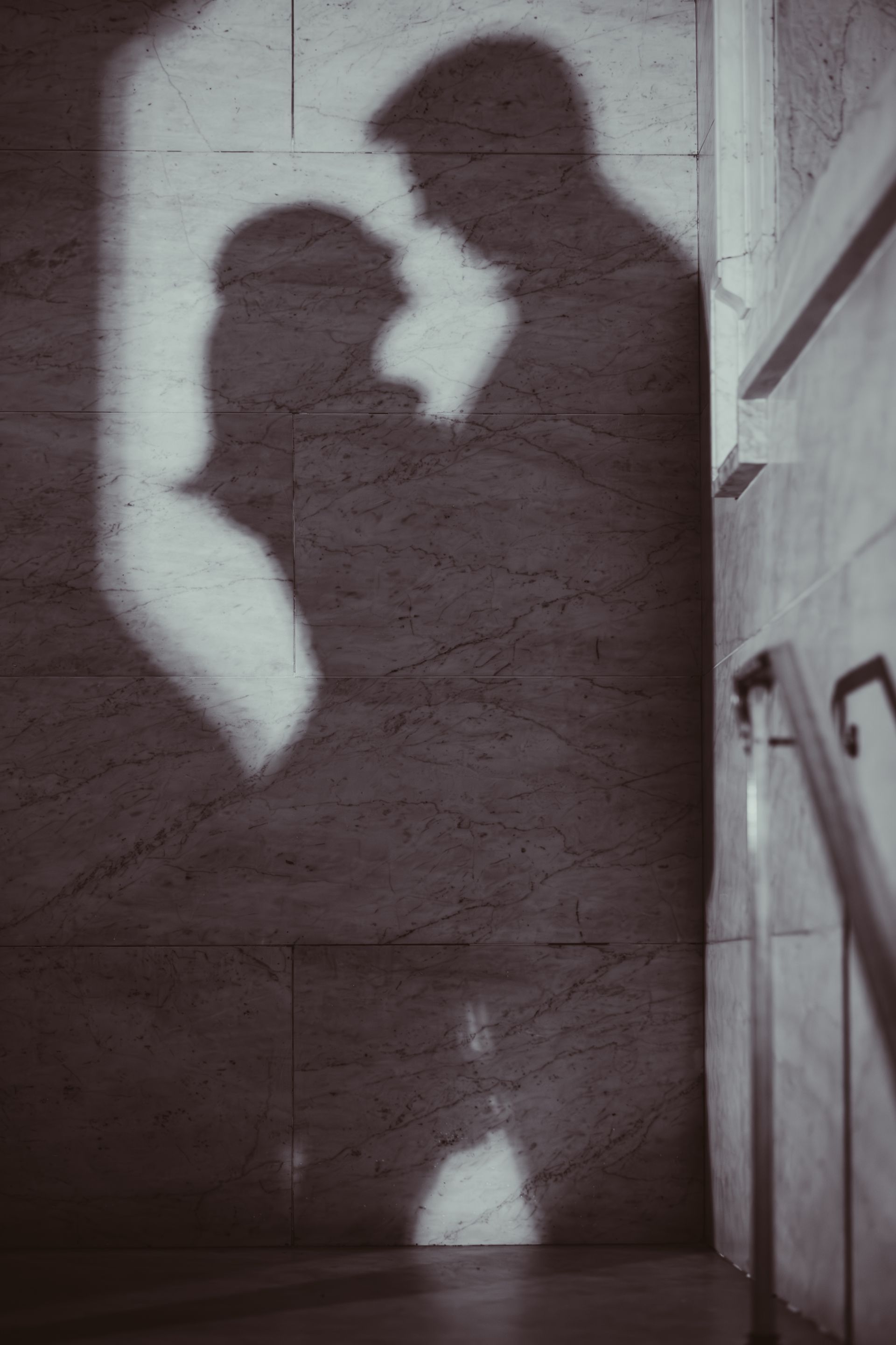 Shadows of two people embracing on a wall, with one holding the other’s face.