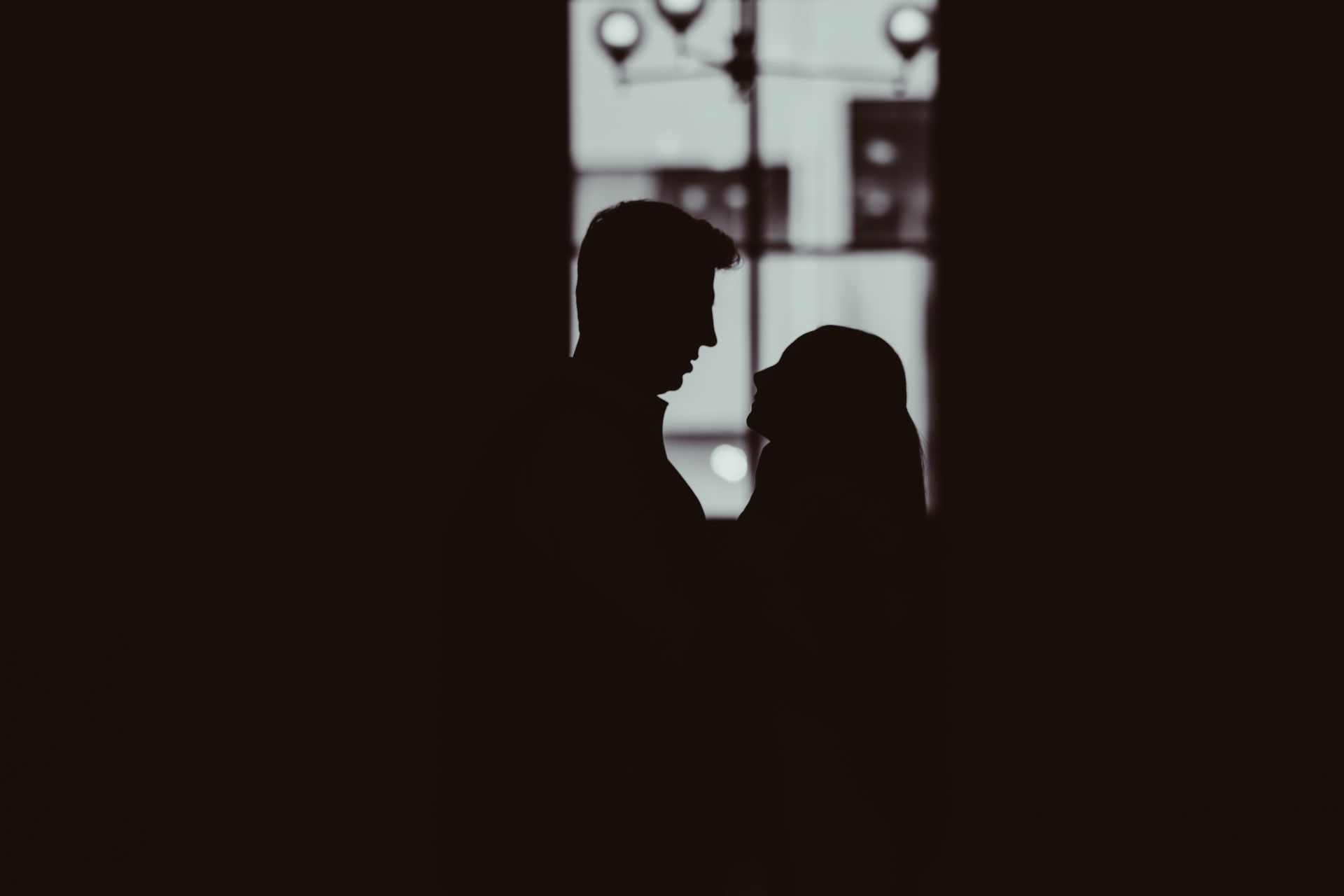 A dark silhouette of two people facing each other against a blurred, light-filled window.