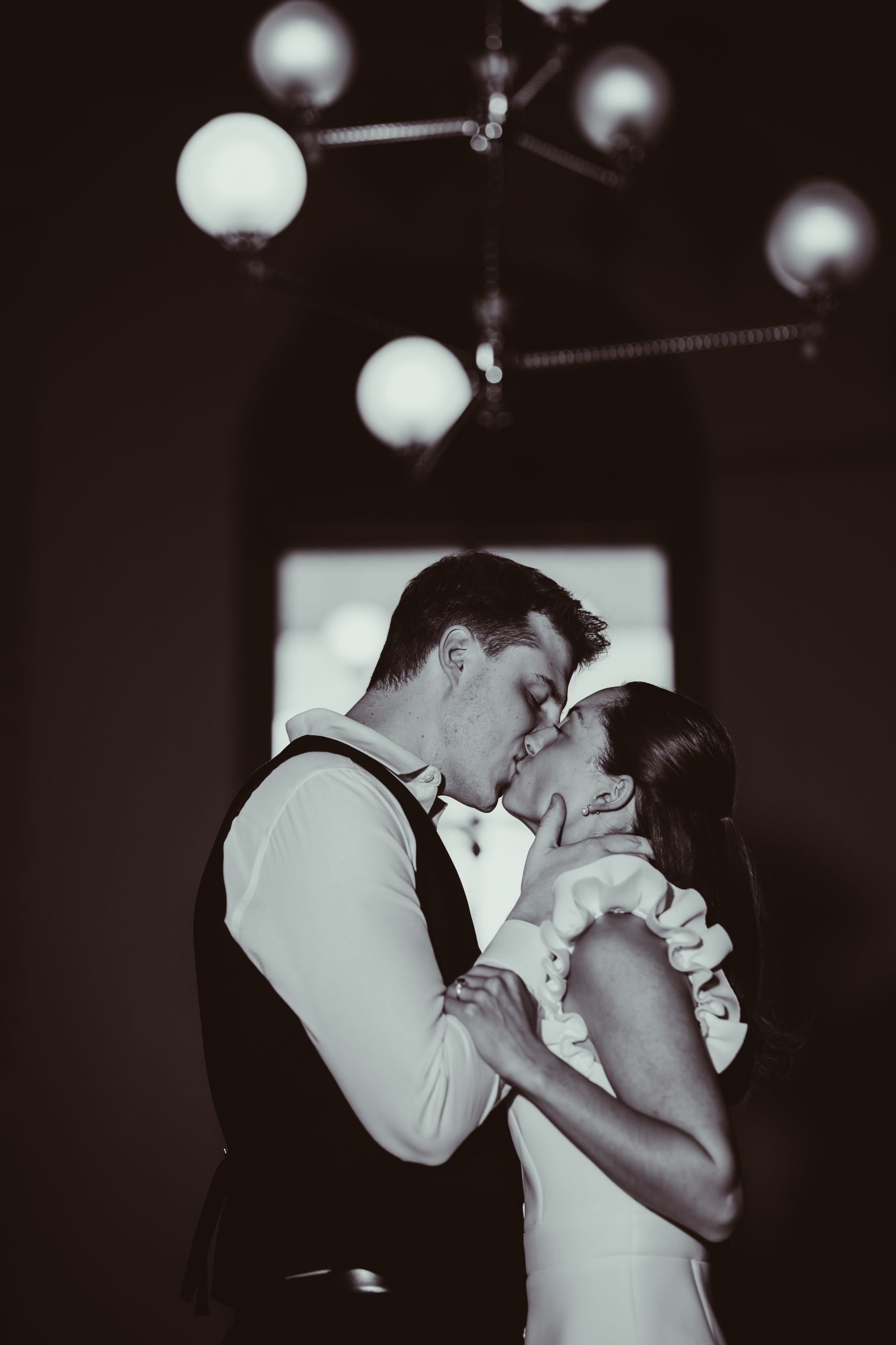 Couple dancing closely and kissing in a dimly lit room with hanging globe lights.