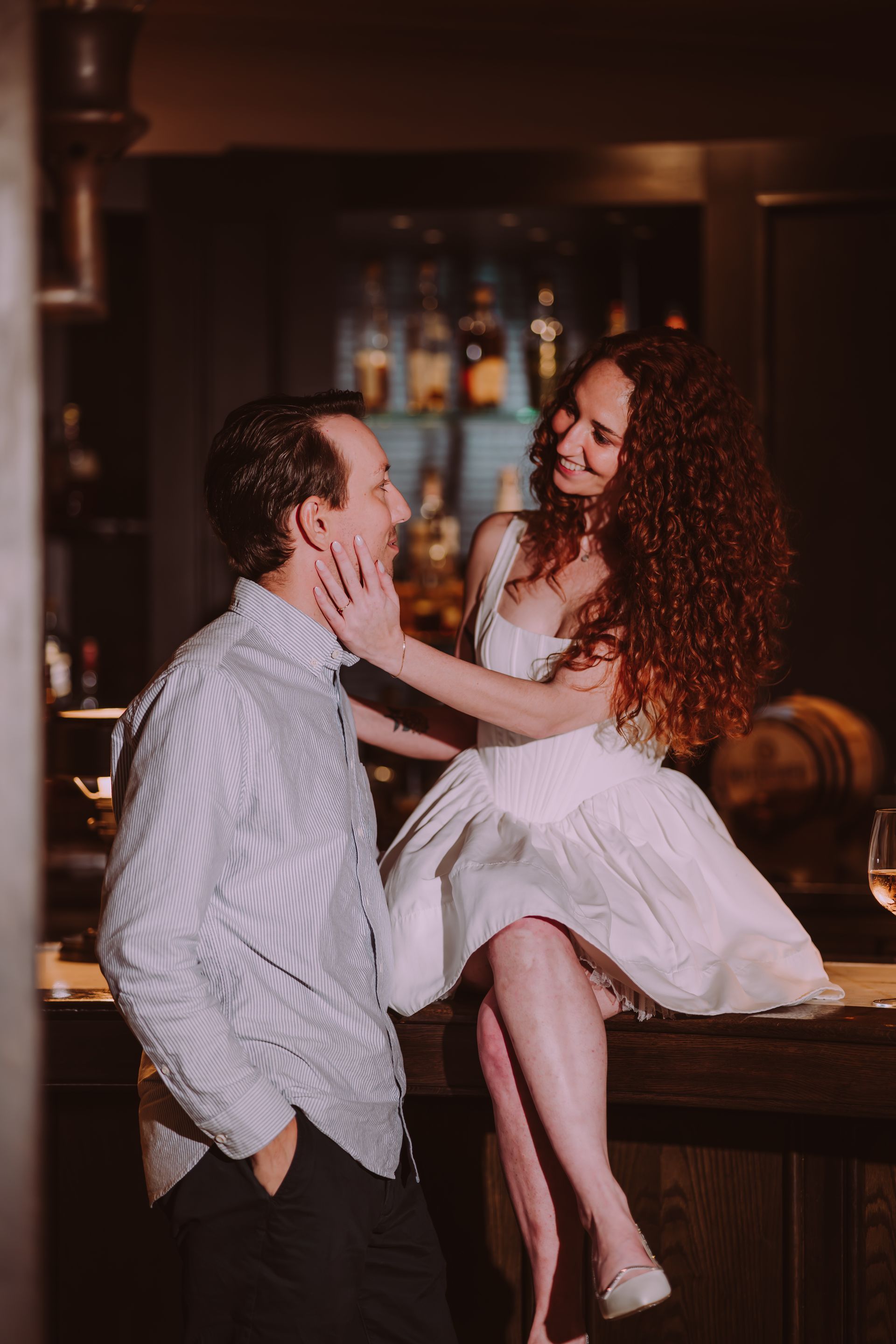 A bride and groom are sitting at a bar toasting with wine glasses.