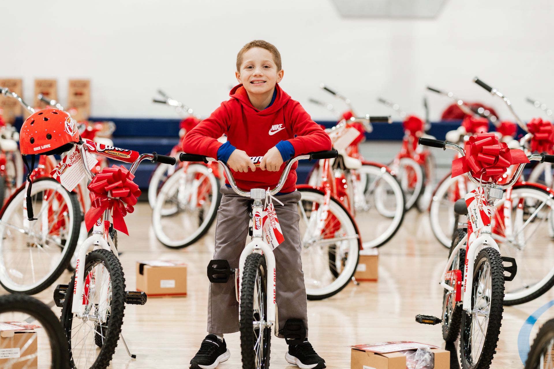 A young boy is standing next to a bicycle in a gym.