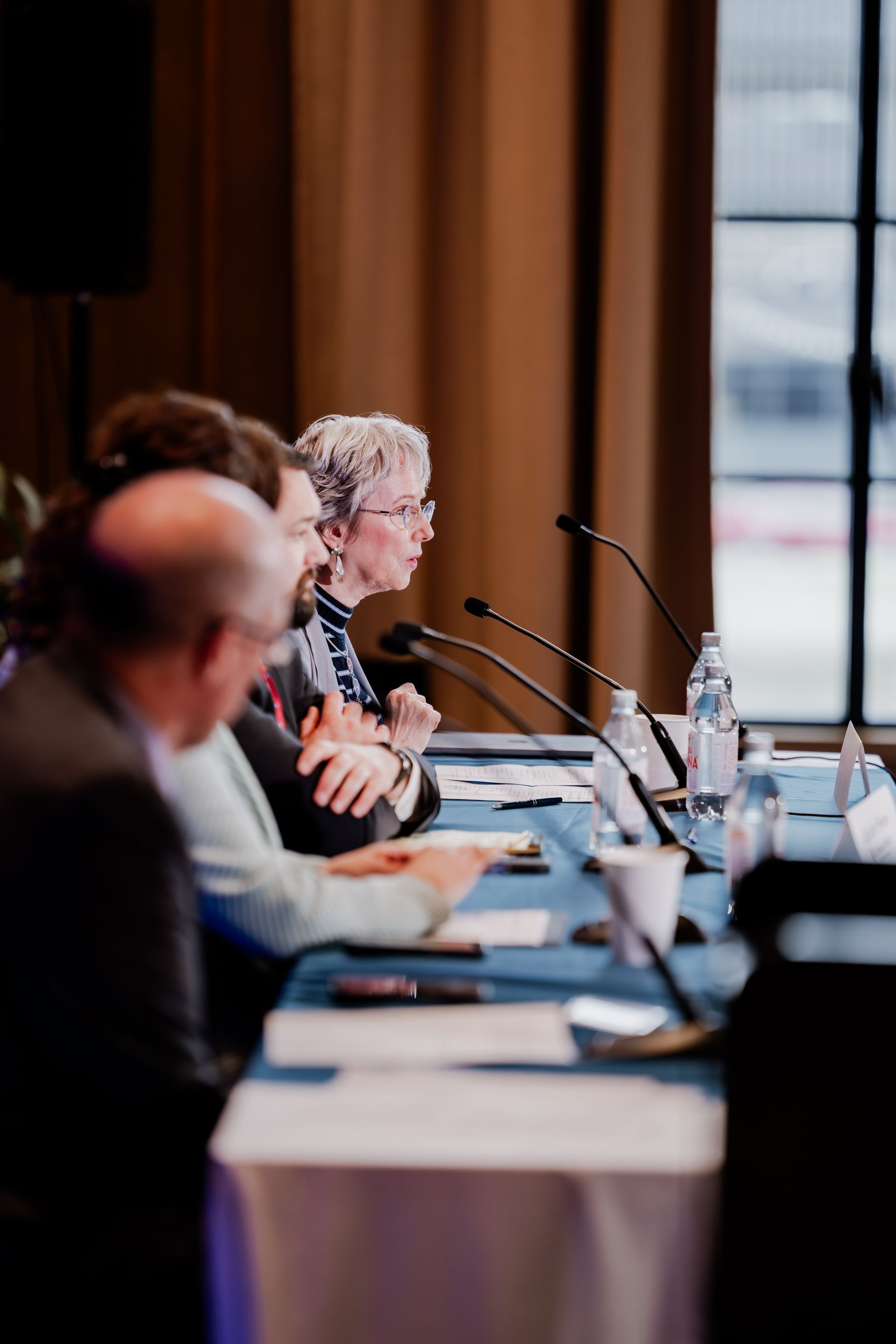 People seated at a table with microphones, likely at a conference or panel discussion, indoors.
