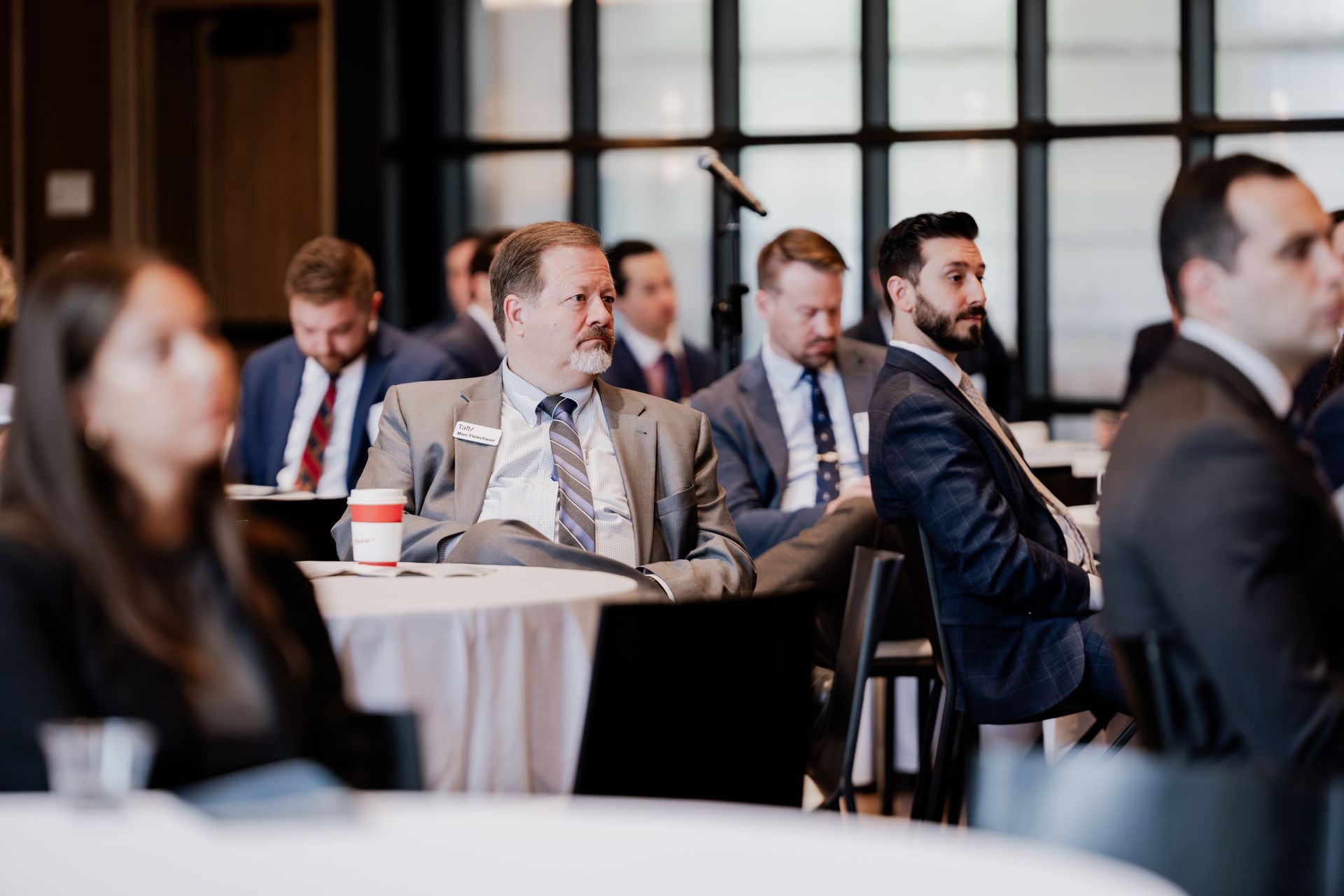 A group of people in suits and ties are sitting at tables in a conference room.