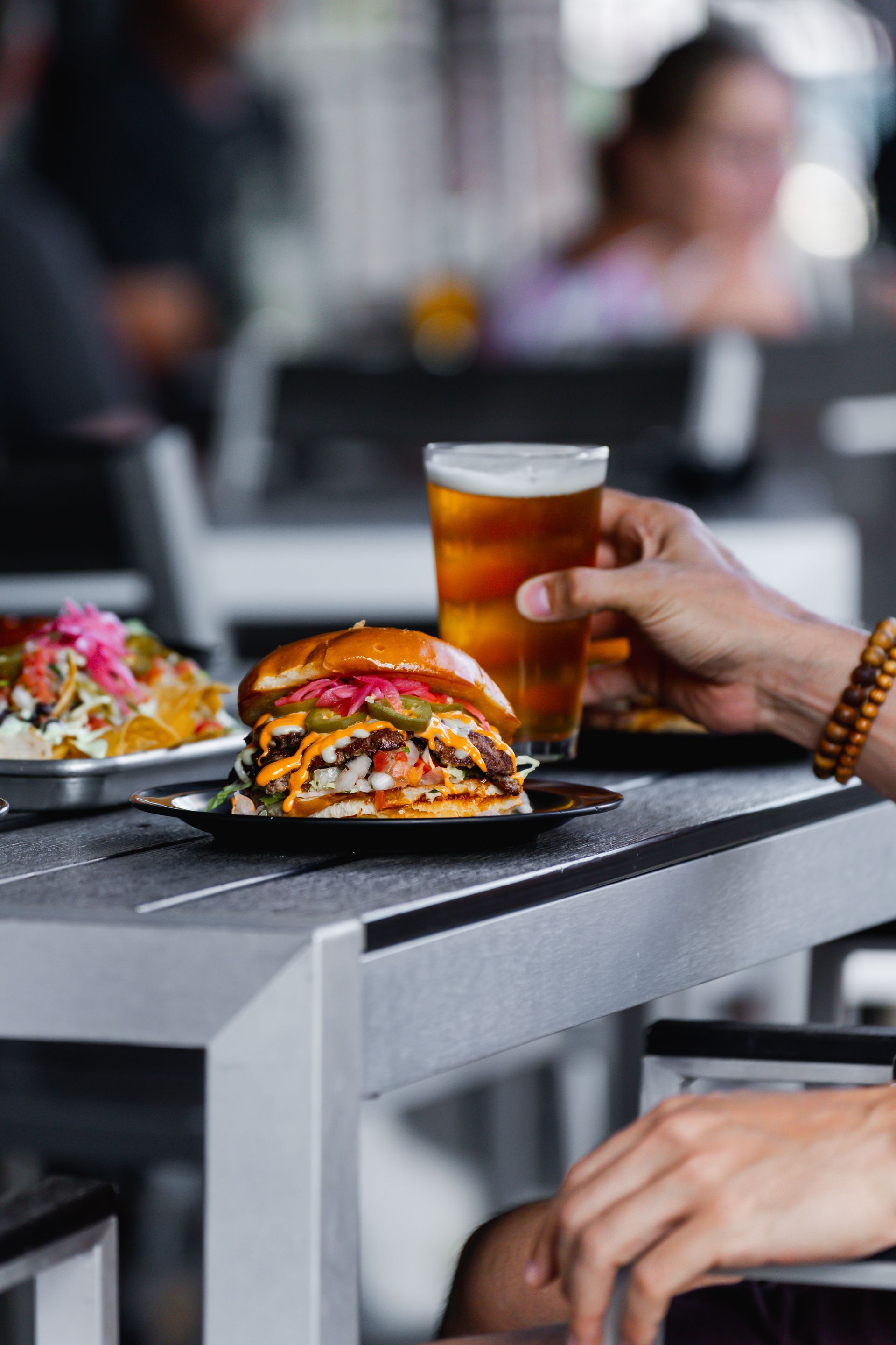 A person is holding a glass of beer next to a plate of food.