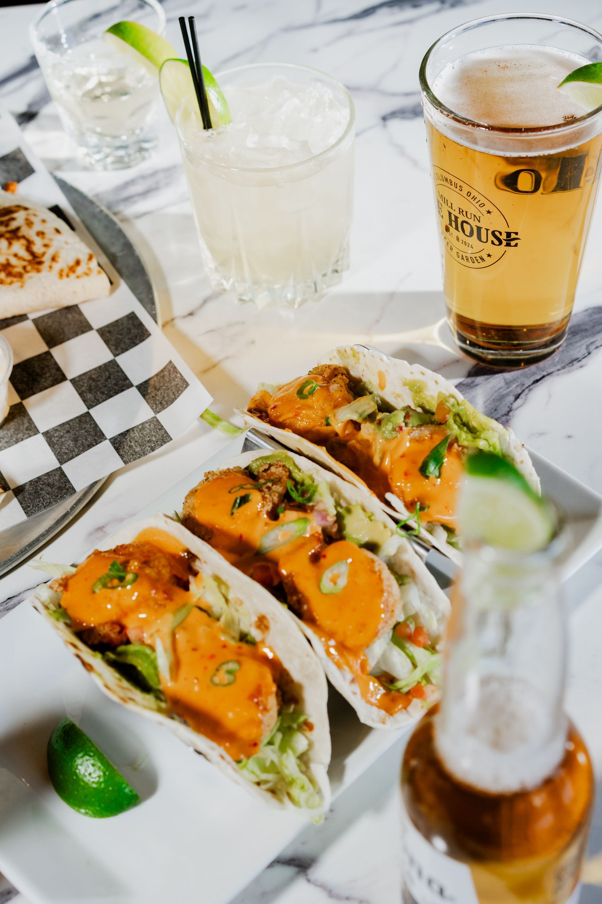 Tacos with drinks: margarita, beer, and shot of liquor on a marble table with a quesadilla.