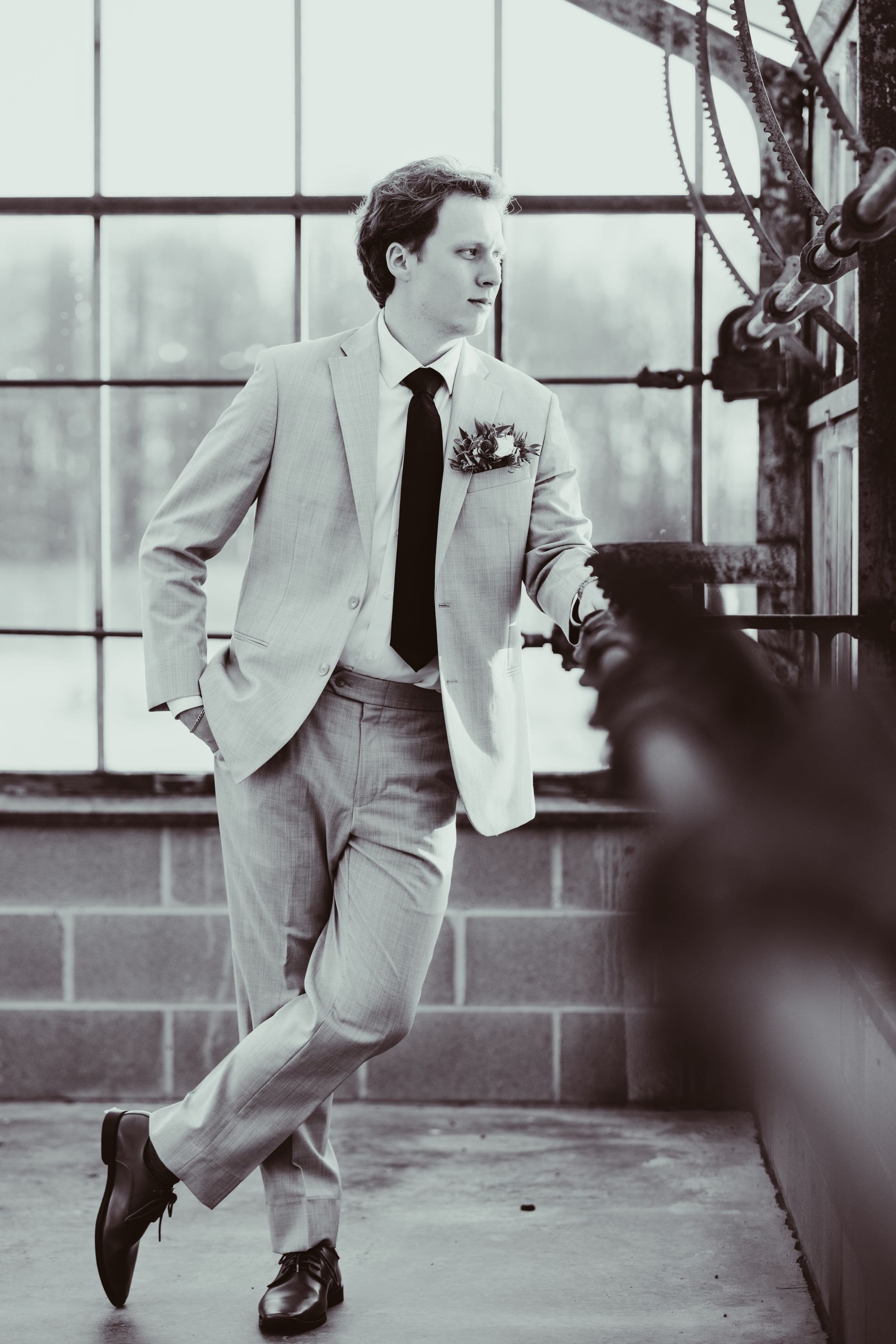 Man in light gray suit and black tie, leaning near a window, black and white.