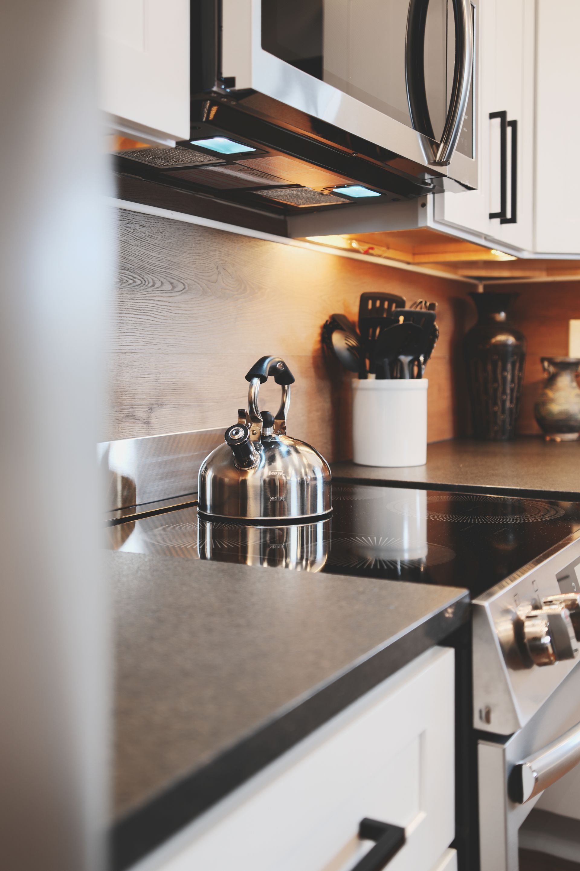 A kitchen with a stove , microwave , and tea kettle on the counter.