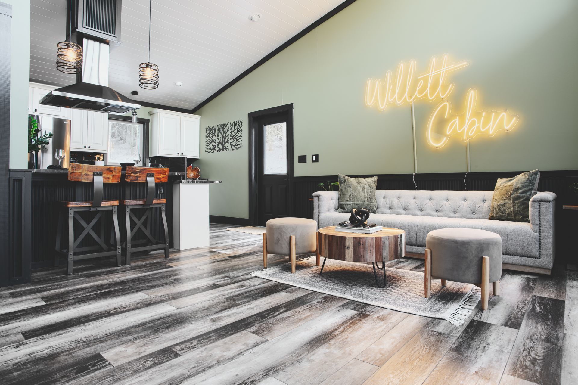 A living room with a couch , coffee table , ottomans and a neon sign that says white cabin.