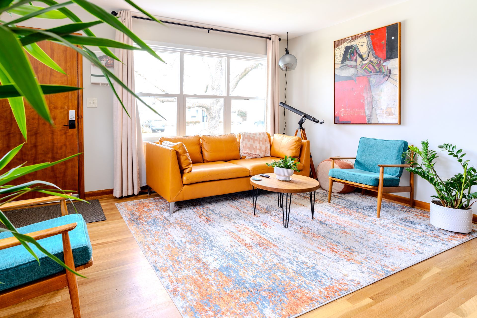 A living room with a yellow couch , blue chairs , and a rug.