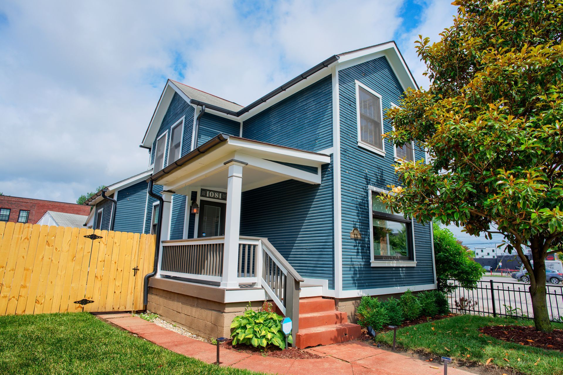 A blue house with a porch and a wooden fence in front of it.