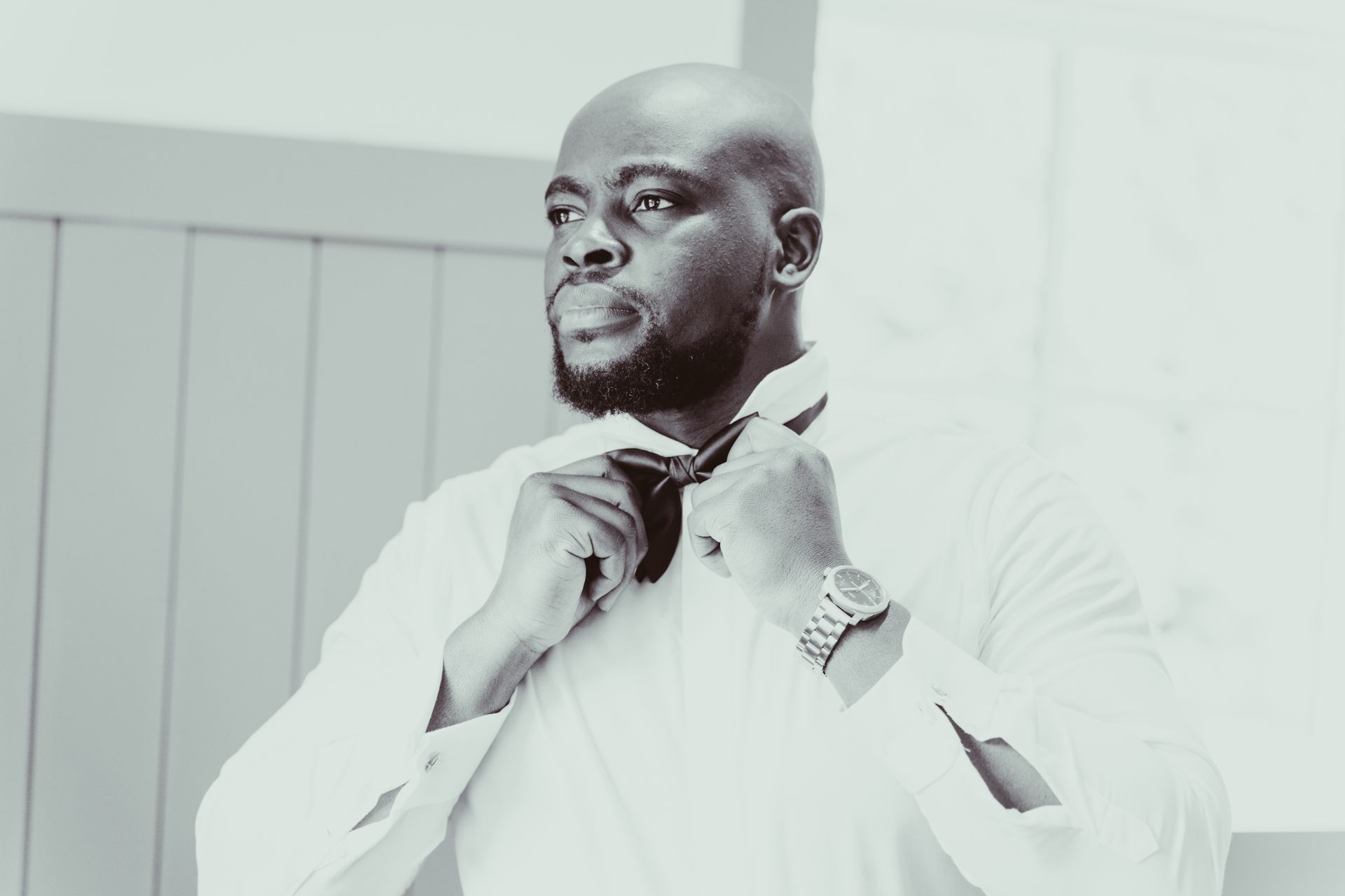 A groom in a white shirt is tying his tie.