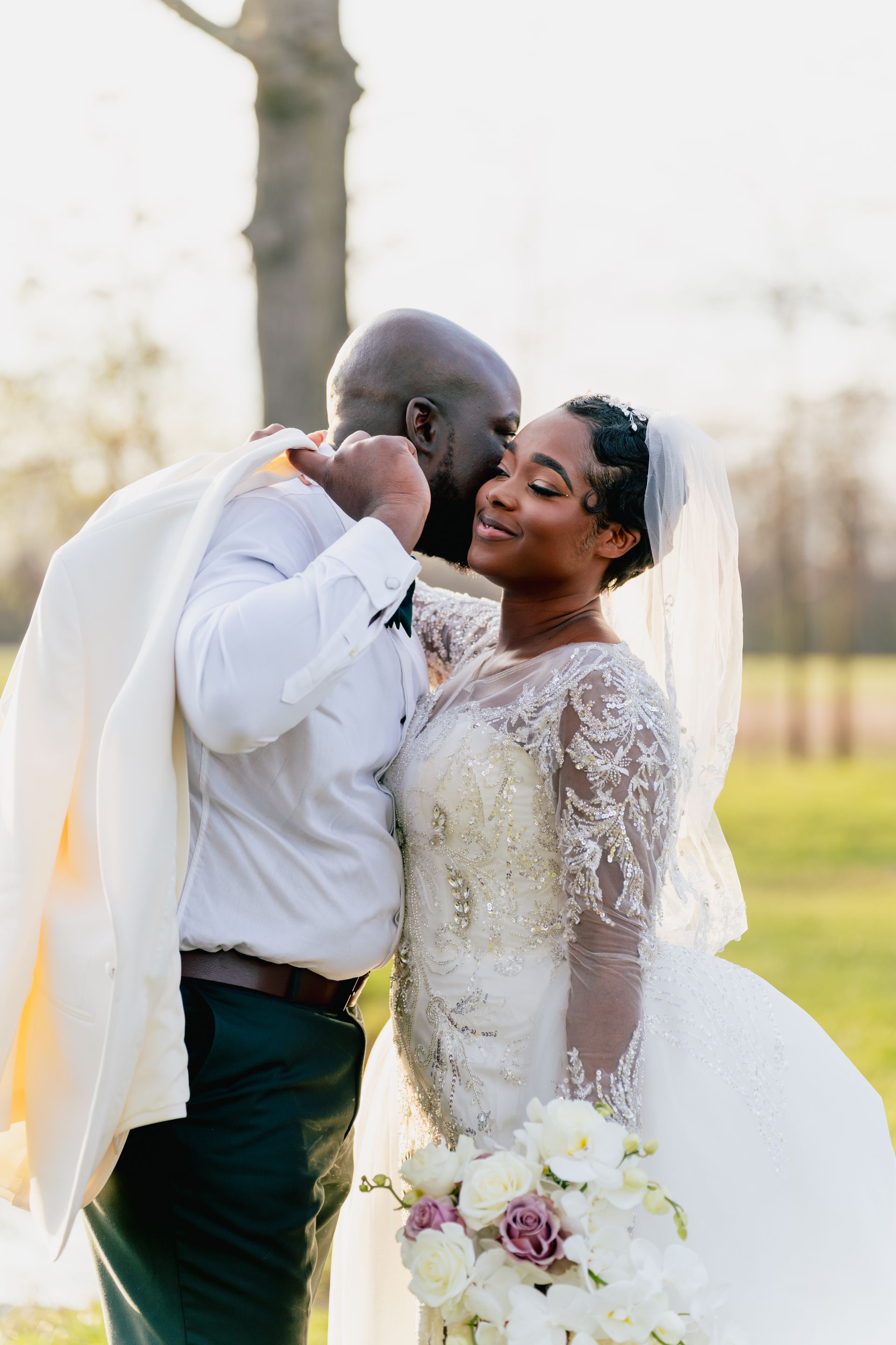A bride and groom are kissing in a park on their wedding day.