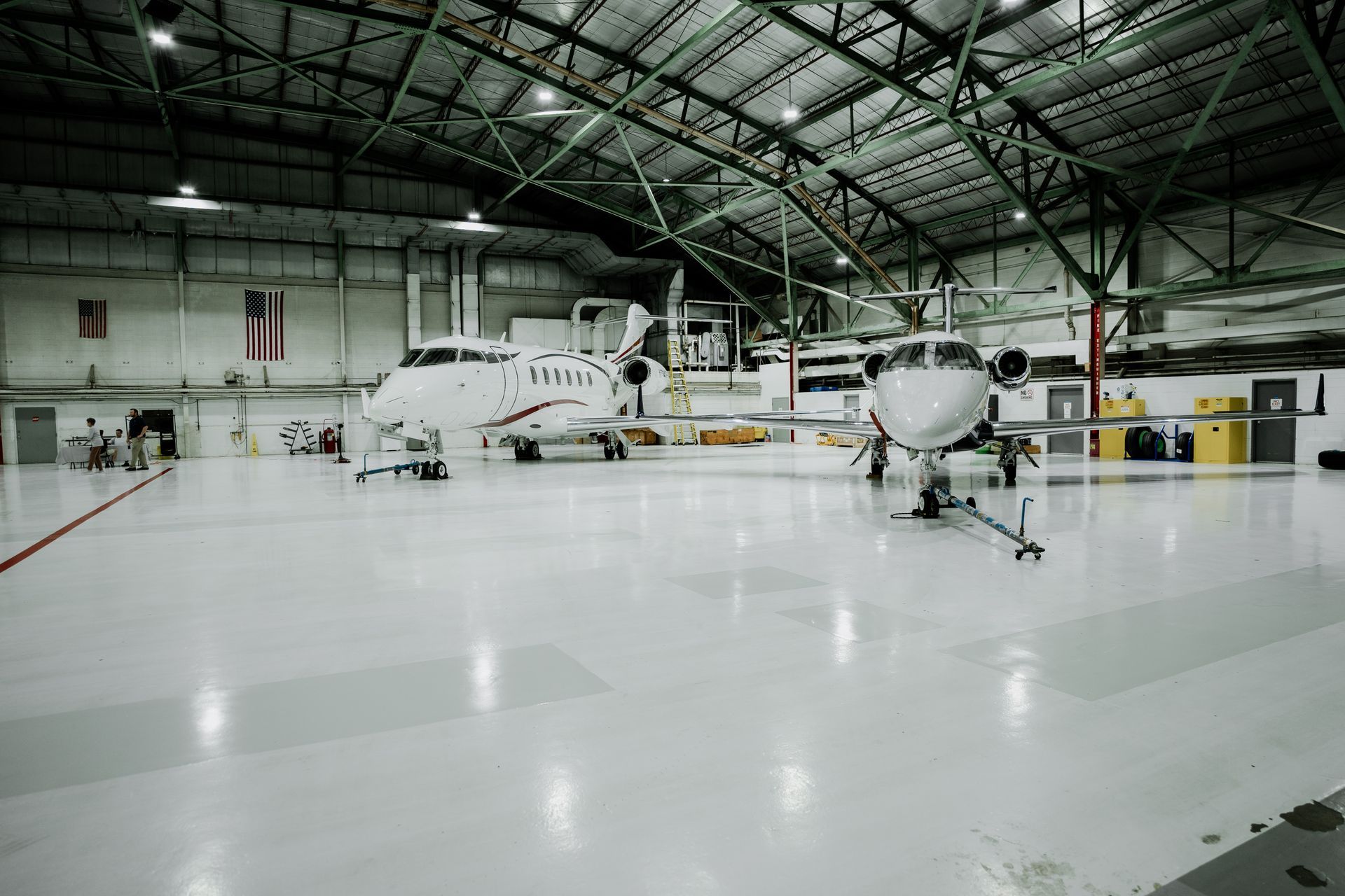 Two private jets inside a large hangar with a shiny white floor.