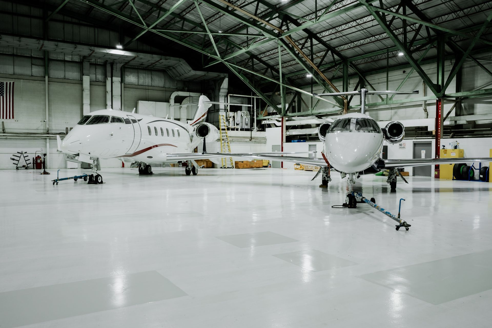 Two white private jets inside a large hangar with a polished floor.