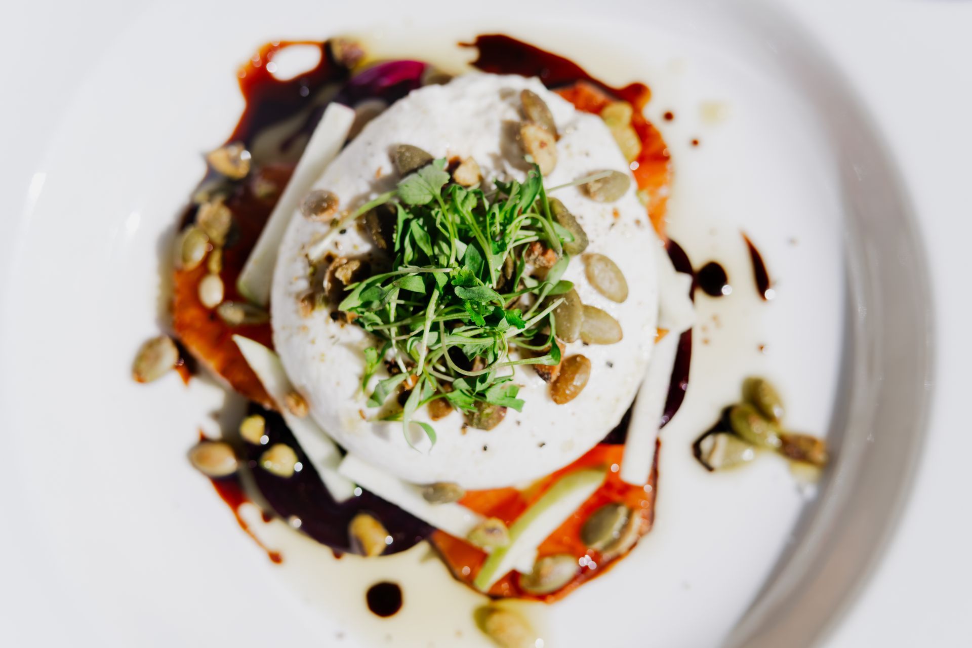 Burrata cheese with pumpkin seeds and greens on a tomato base, drizzled with balsamic glaze.