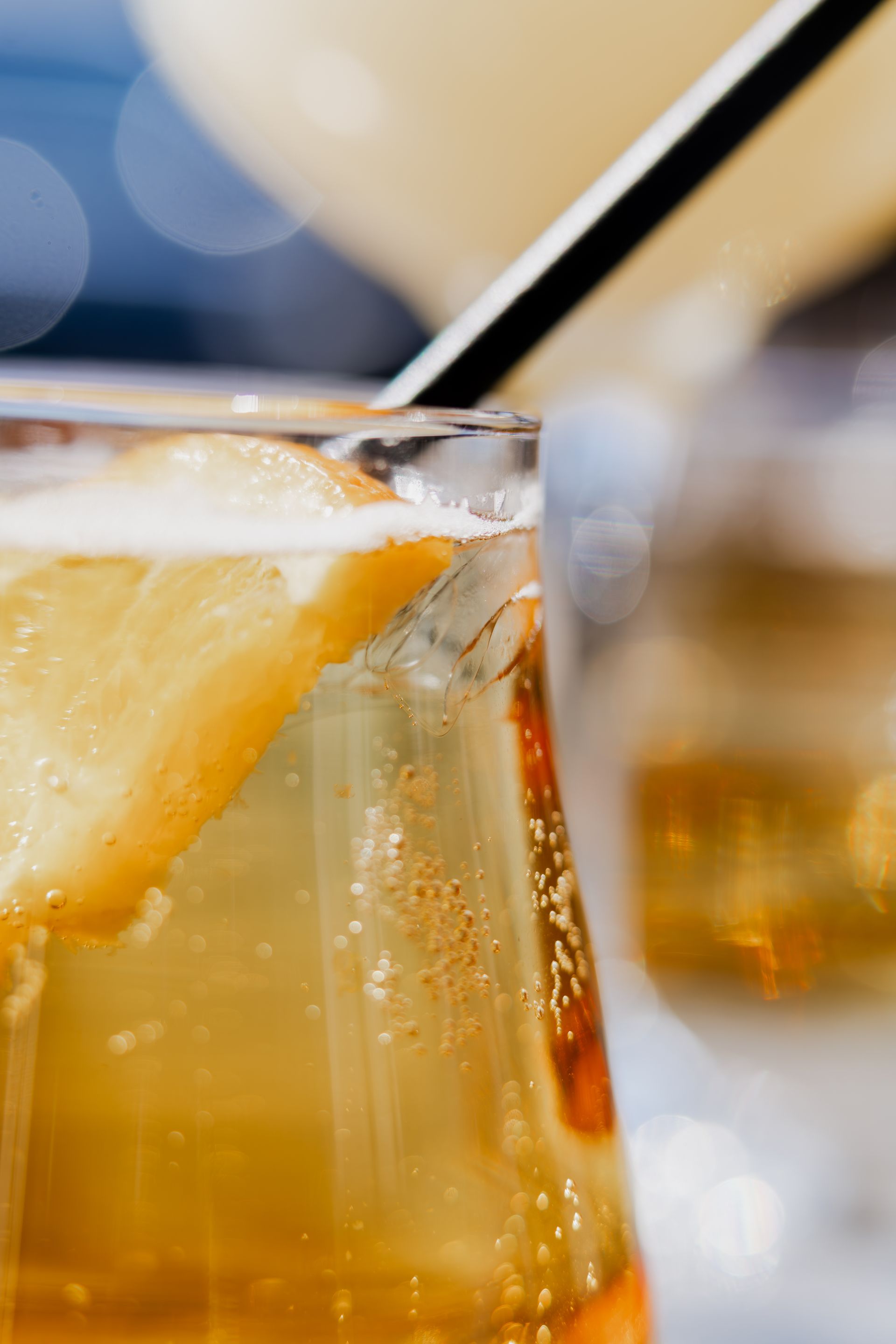 Close-up of a drink with orange slice garnish, bubbly with straw, in focus.