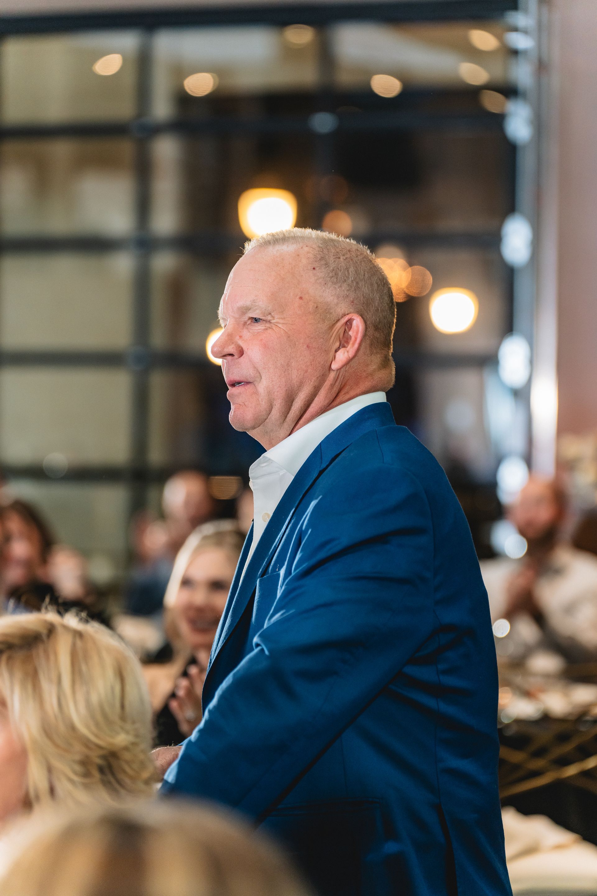 A man in a blue suit is standing in front of a crowd of people.