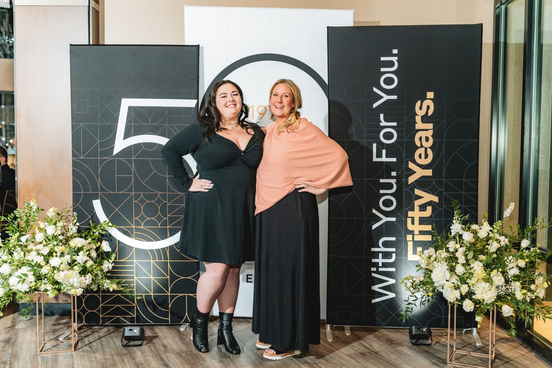 Two women are posing for a picture in front of a sign that says `` with you for fifty years ''.