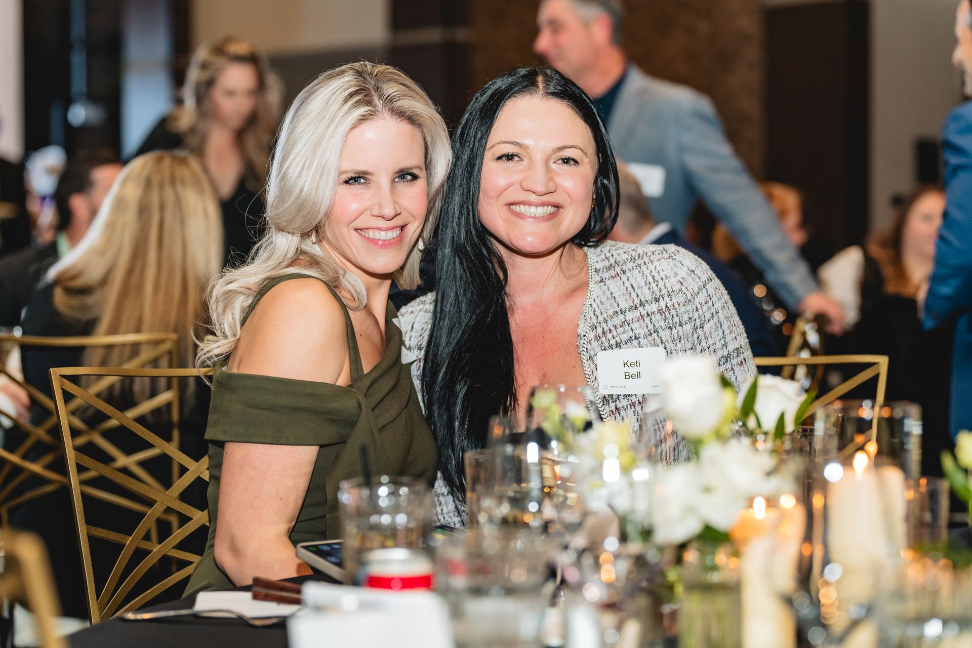 Two women are posing for a picture at a table at a party.