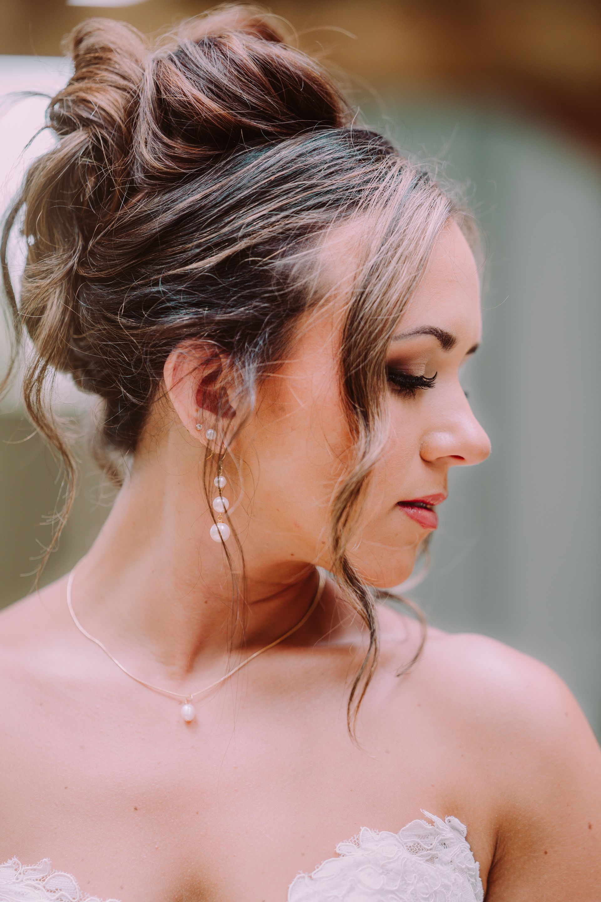 Woman with updo hairstyle, wearing earrings and necklace, looking down with a soft expression.