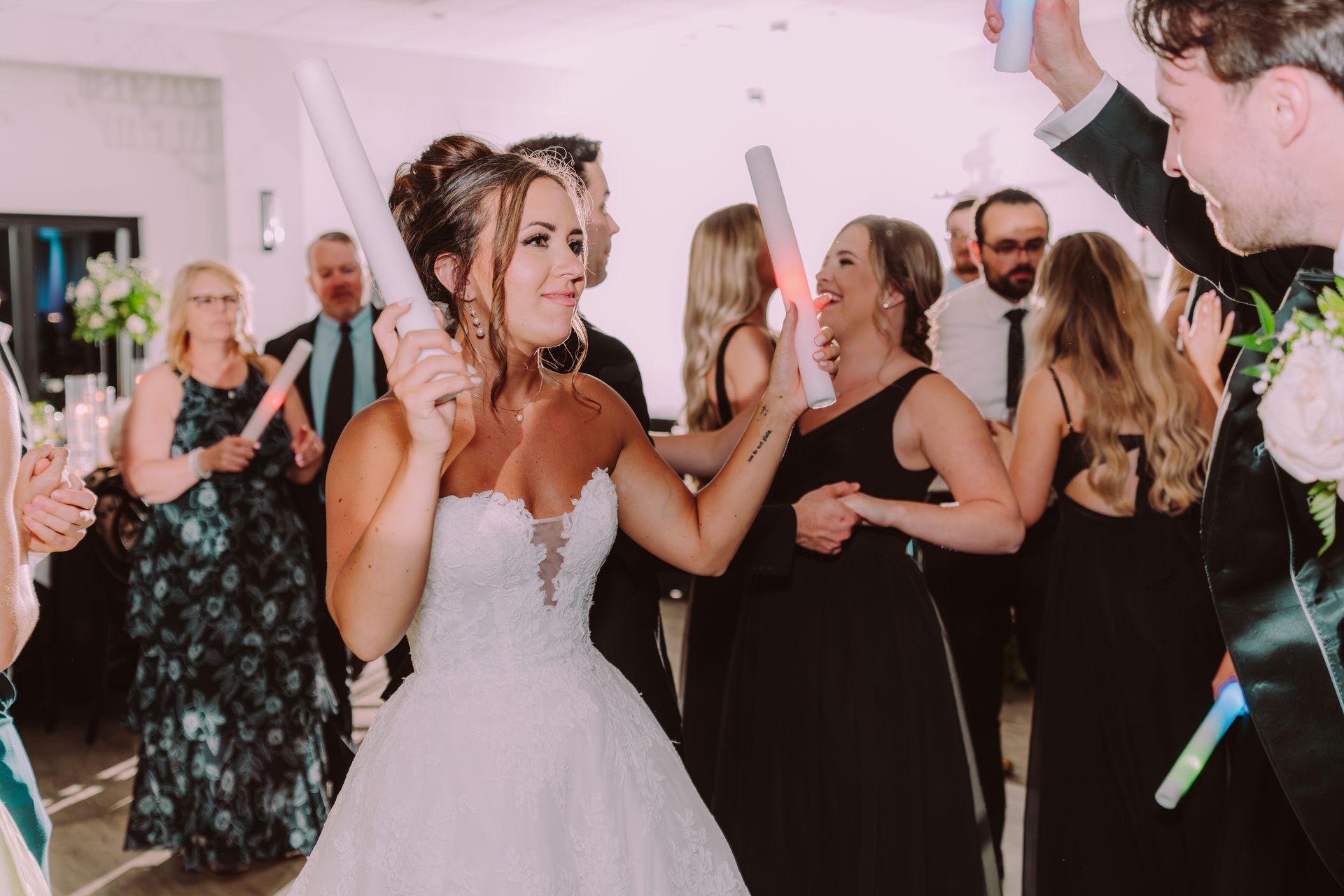 Bride and guests dancing at a wedding reception, waving glowing sticks. 