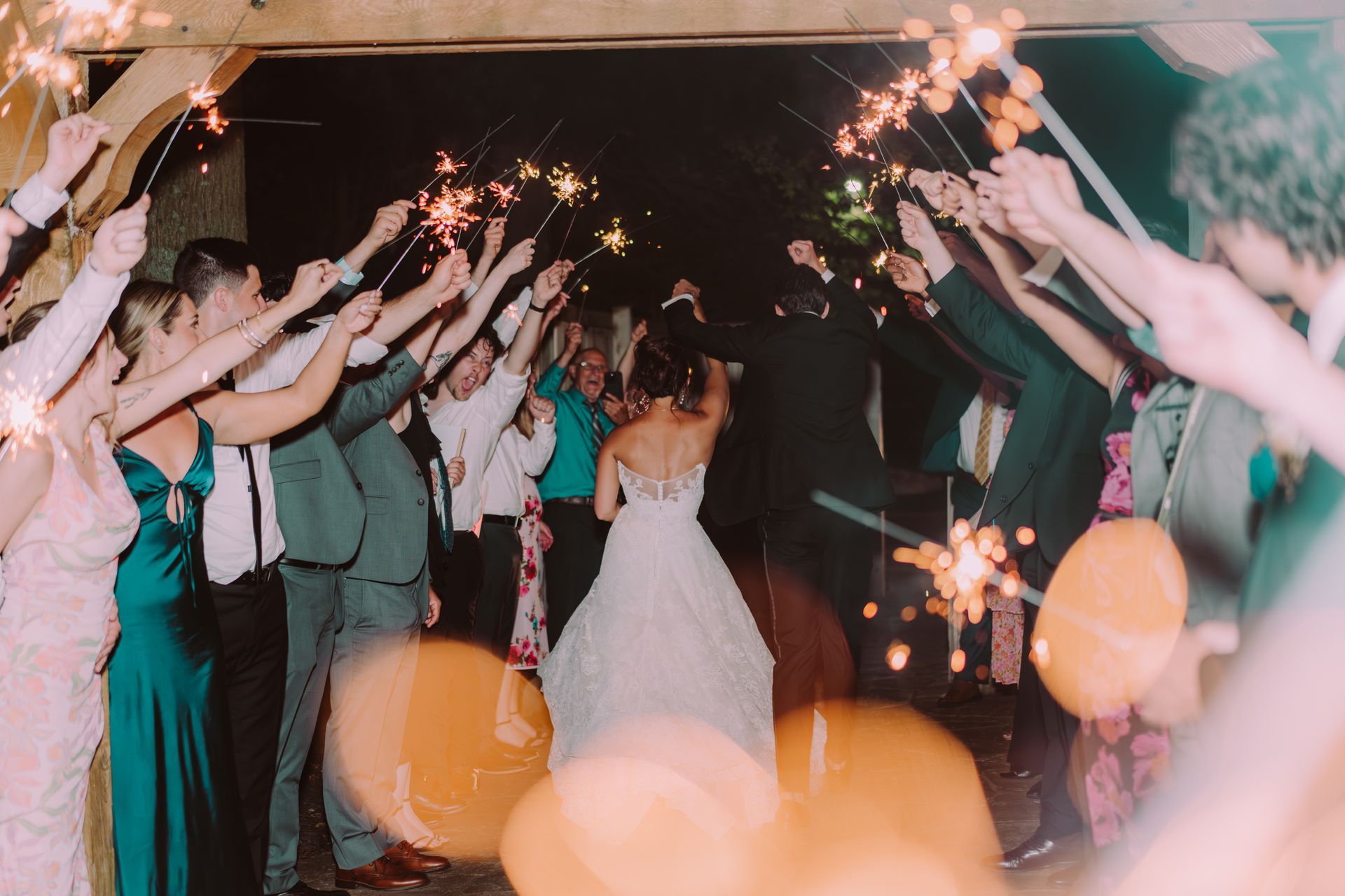 Bride and groom exit a wedding, cheered on by guests holding lit sparklers.