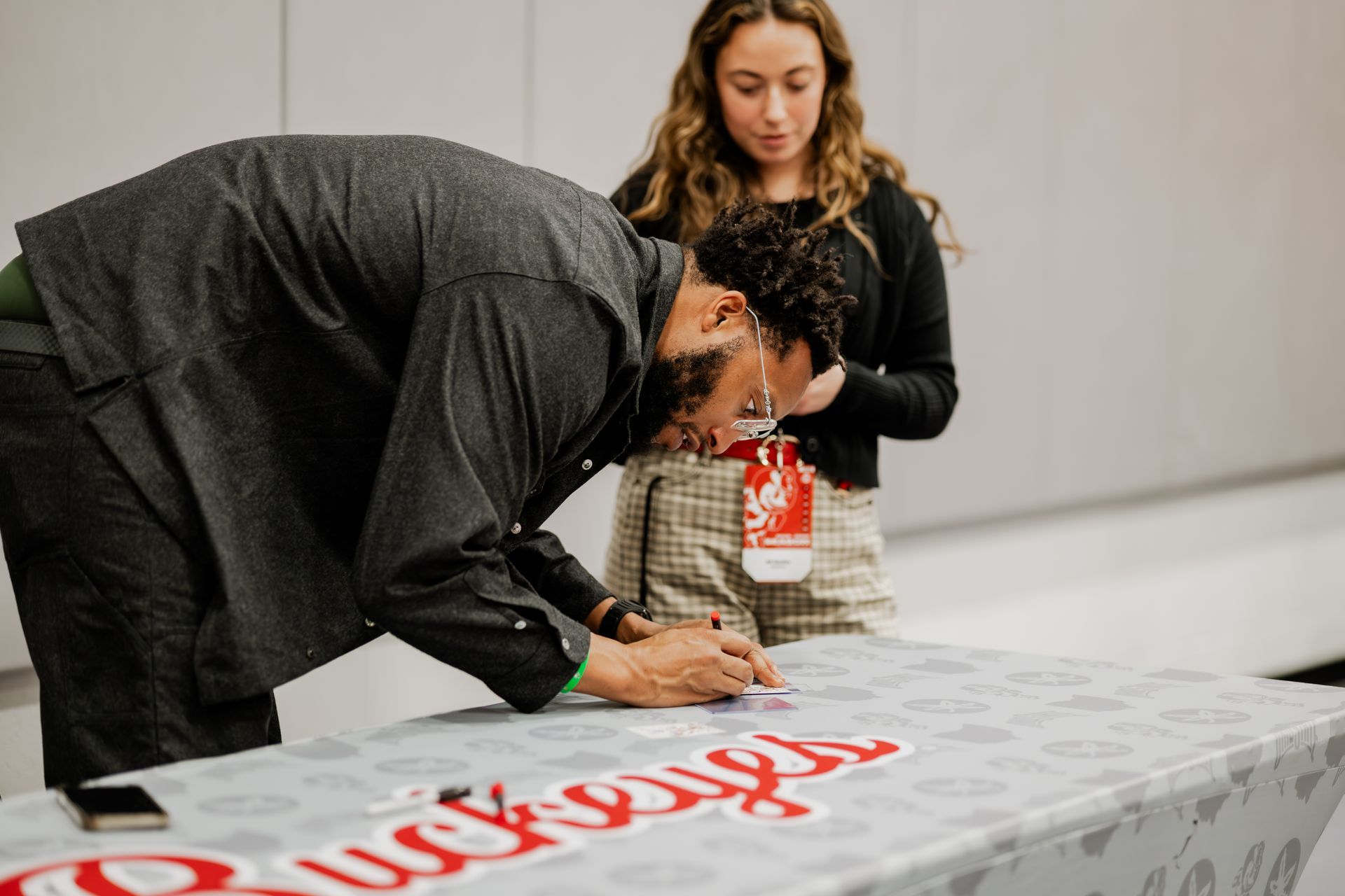 Man signs item on table labeled “Buckeyes,” woman and child stand behind.Midwest Cards | Event Photography
