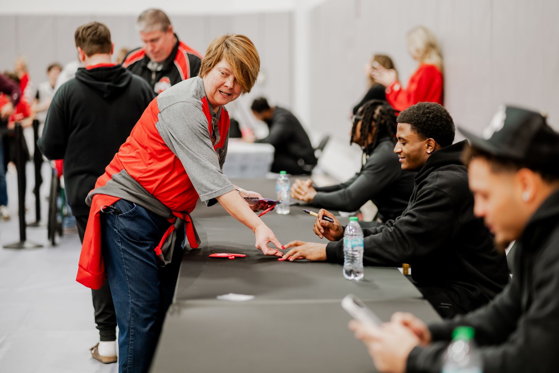 A fan reaches toward a player in a red and black setting.Midwest Cards | Event Photography