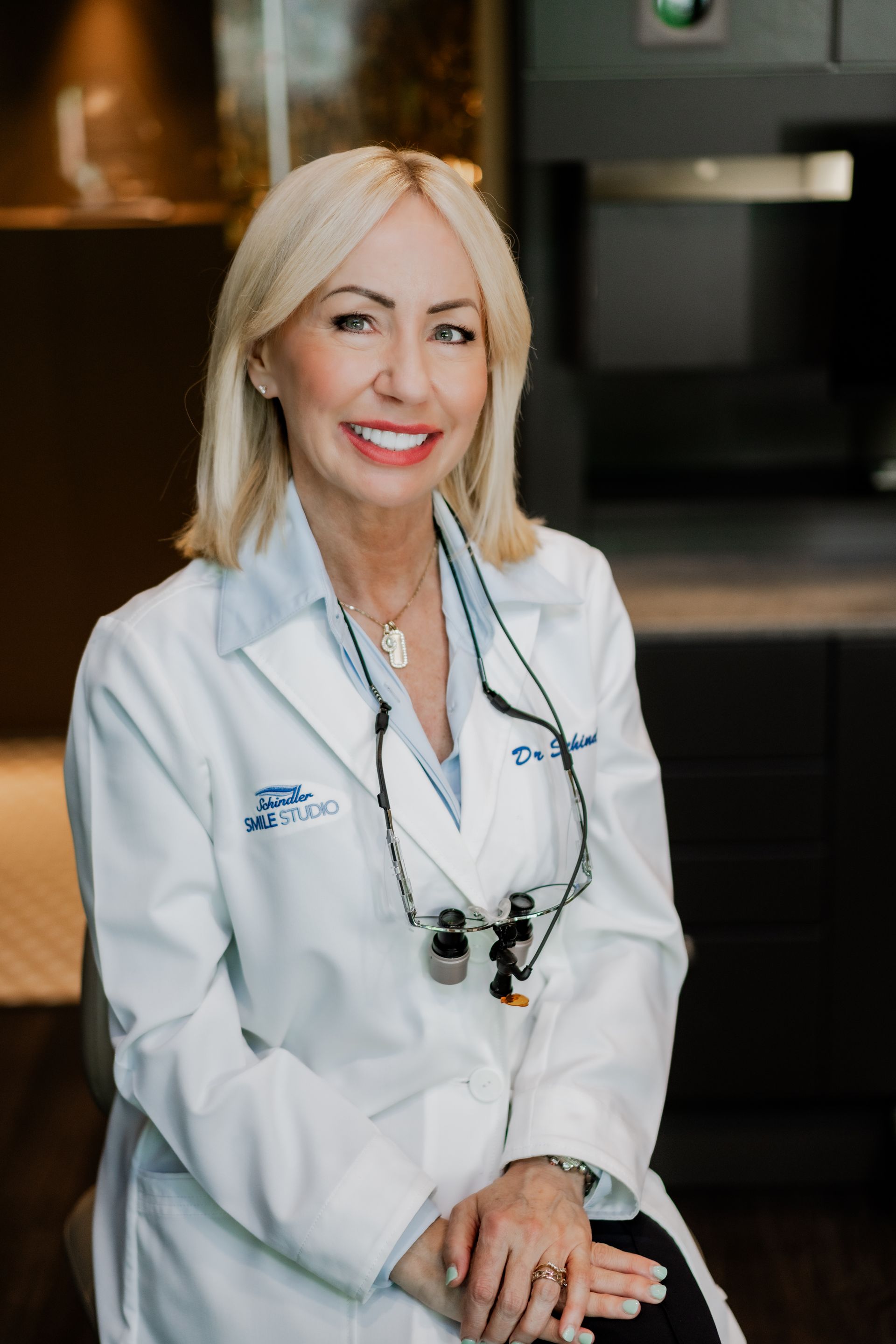 Woman with blonde hair, wearing a lab coat, smiling at the camera.
