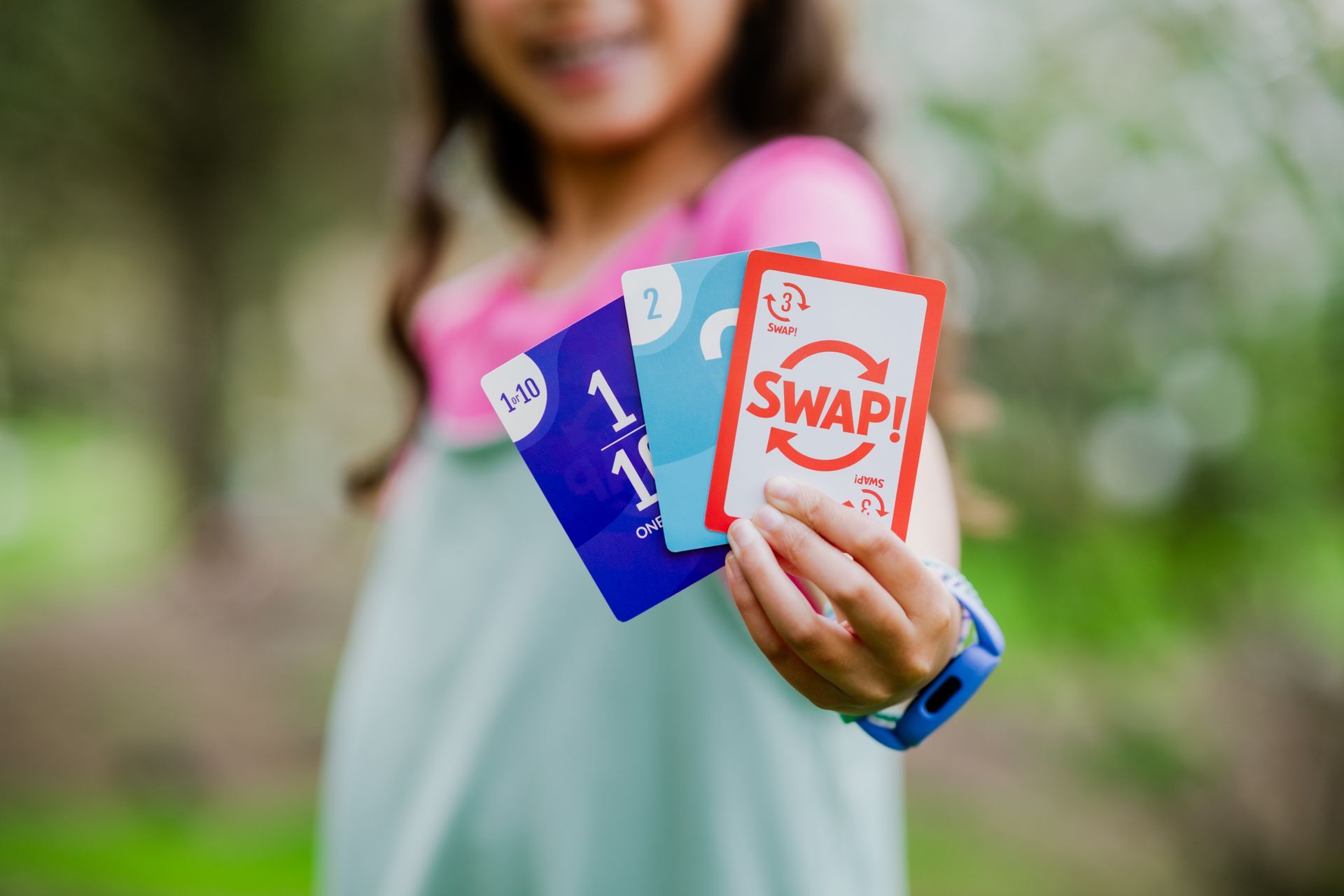 Person holding three colorful SWAP! cards toward the camera outdoors