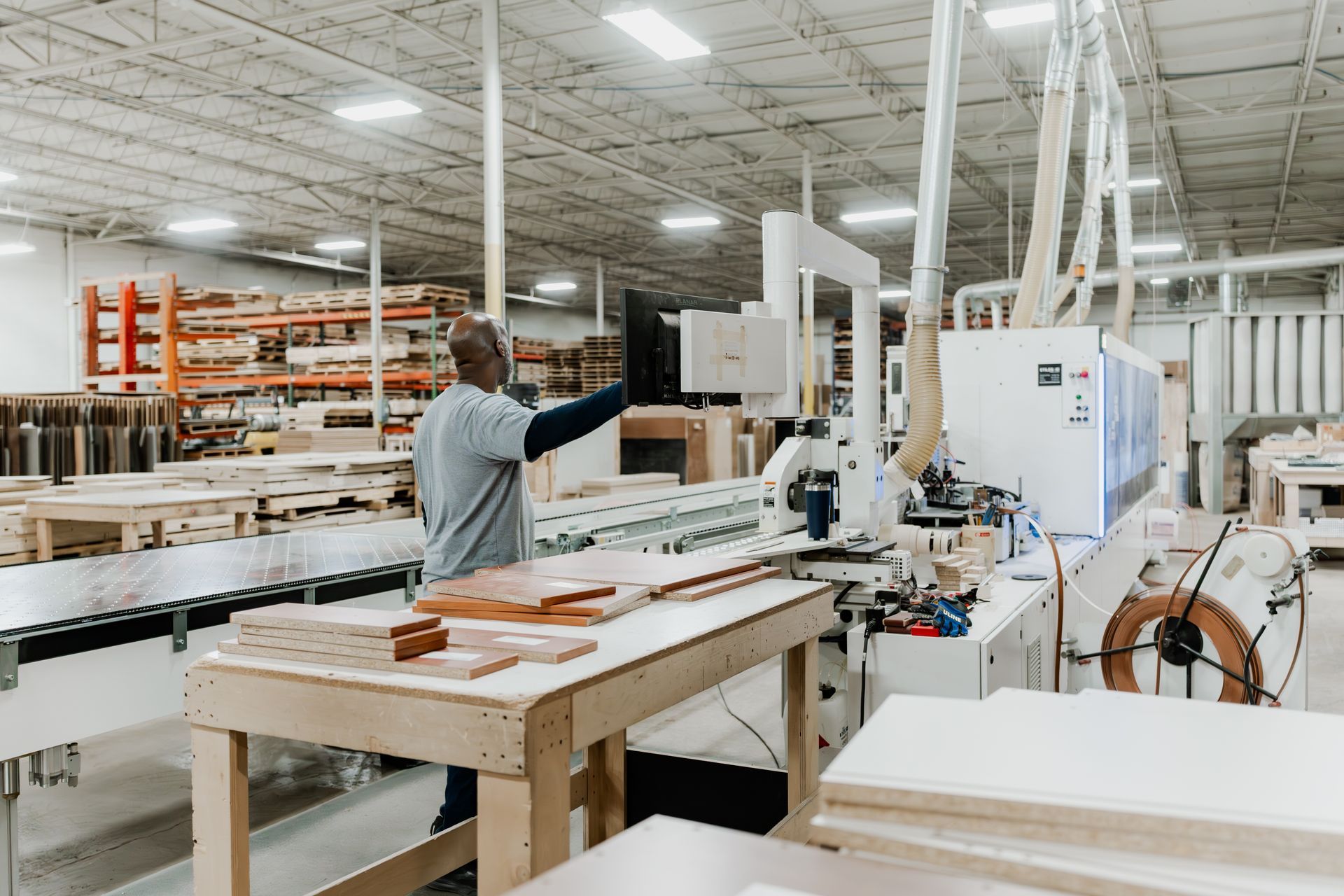 Man operating machinery in a woodworking factory; wooden planks and equipment in the background.