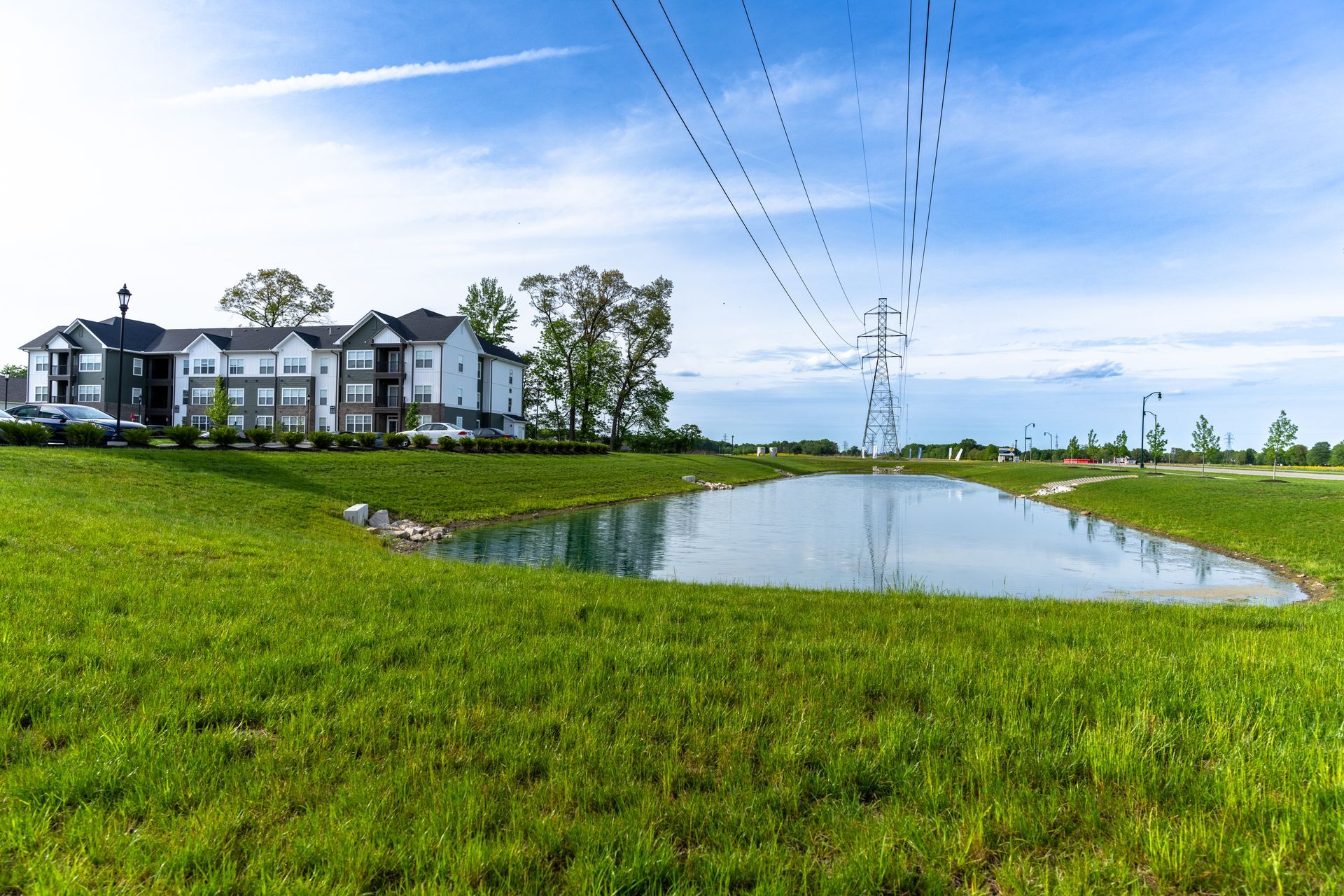 A pond in the middle of a grassy field with a building in the background.