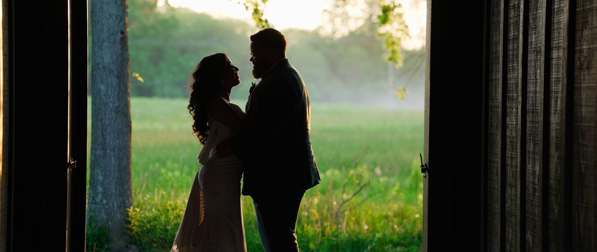 Silhouetted couple embracing in a doorway, bathed in golden sunlight, overlooking a green field.