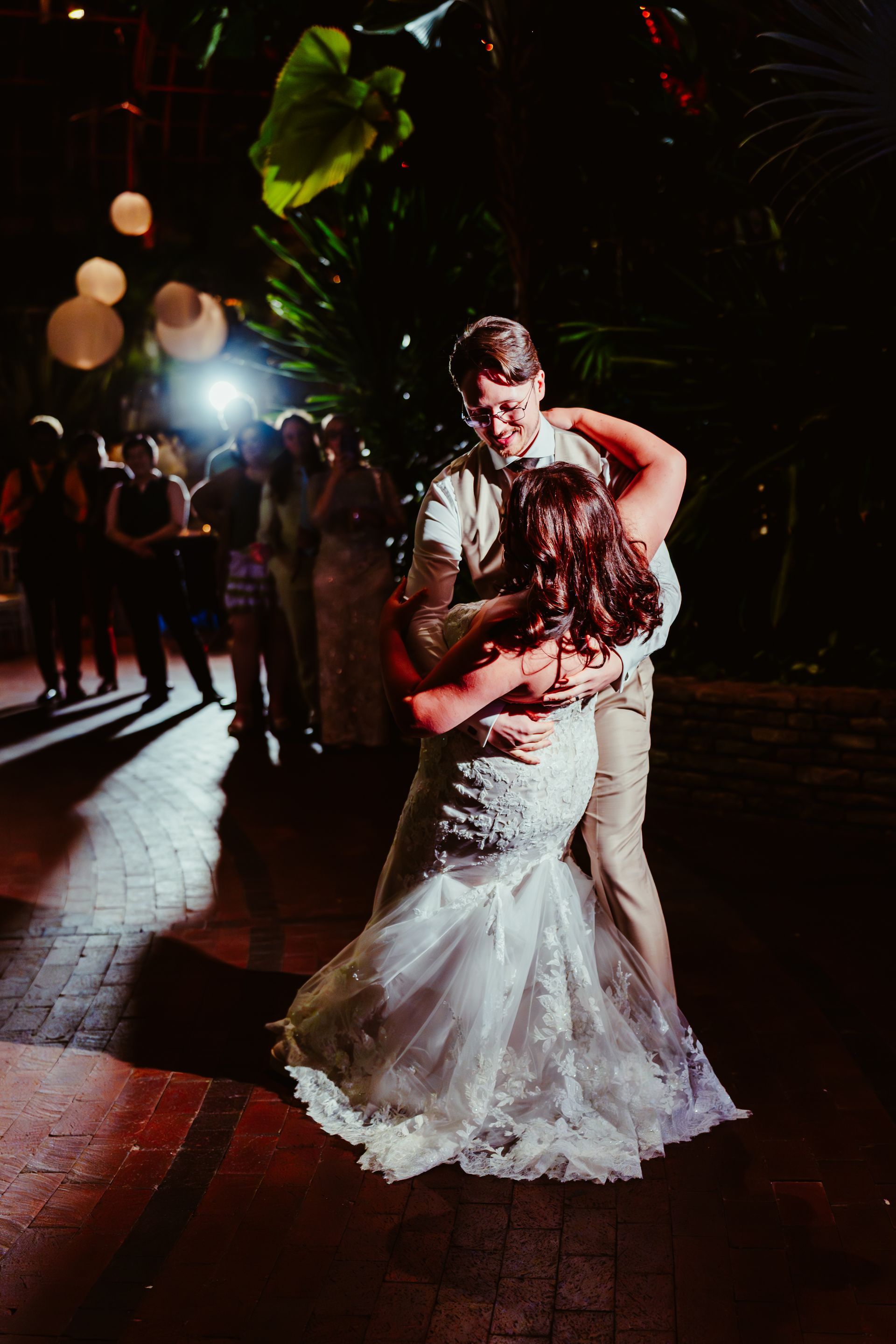 Couple dancing at a wedding reception, woman in white gown, man in tan suit, outdoor setting.